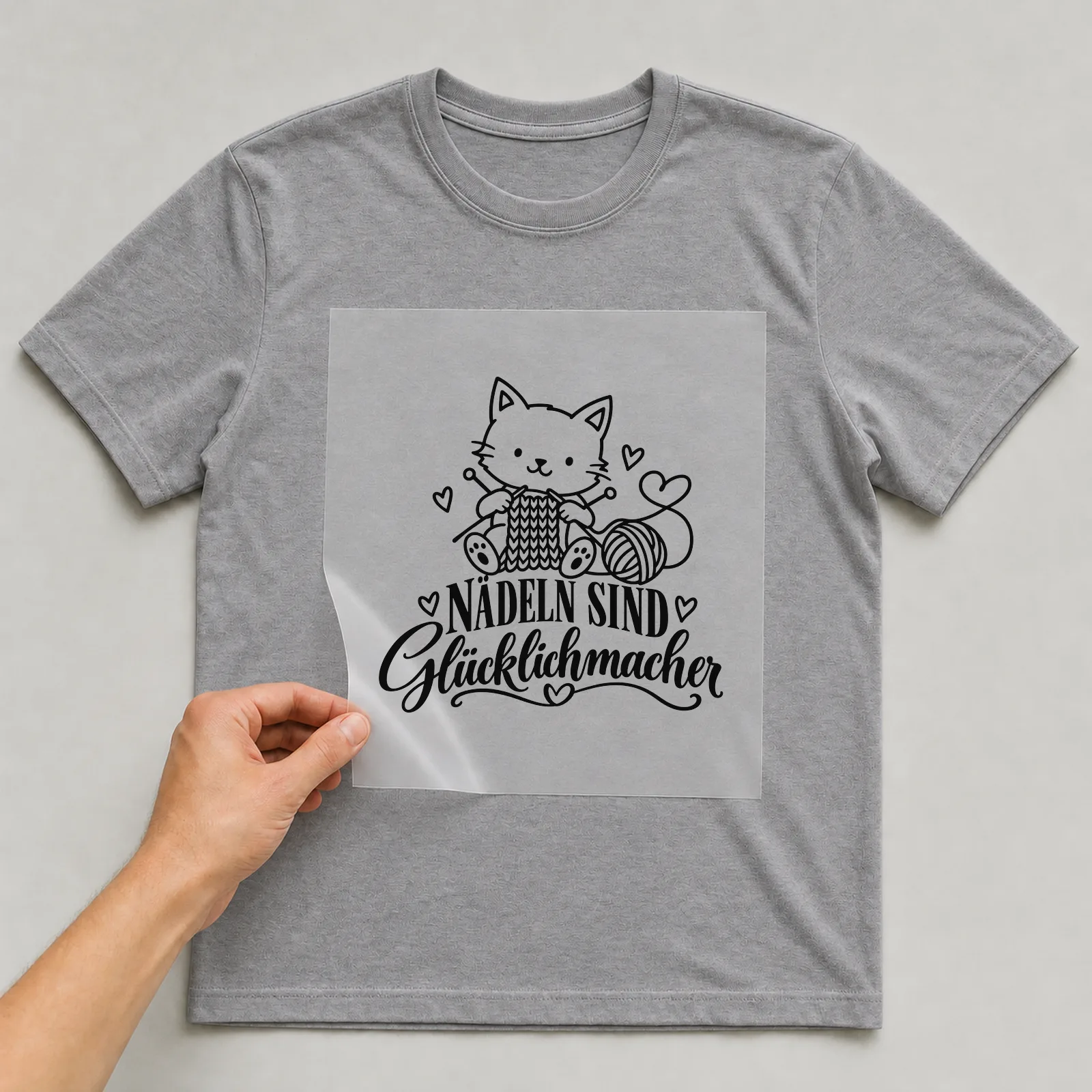 Bügelbild „Nadeln sind Glücklichmacher“ auf grauem T-Shirt, Folie wird aufgelegt