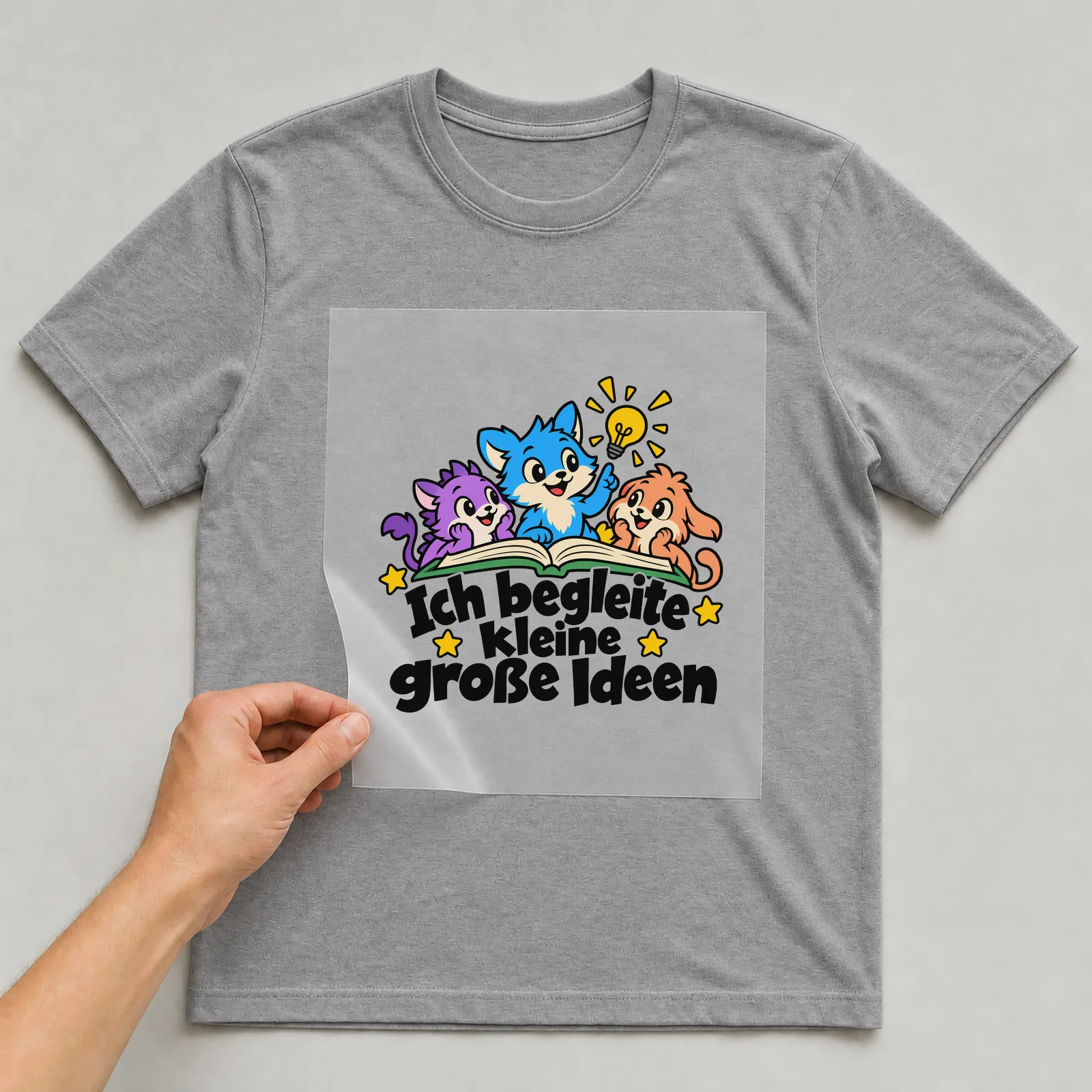 Bügelbild „Ich begleite kleine große Ideen“ auf grauem T-Shirt, Folie wird aufgelegt