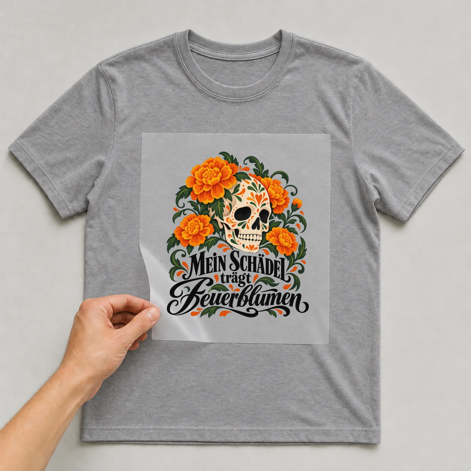 Bügelbild „Mein Schädel trägt Feuerblumen“ auf grauem T-Shirt, Folie wird aufgelegt