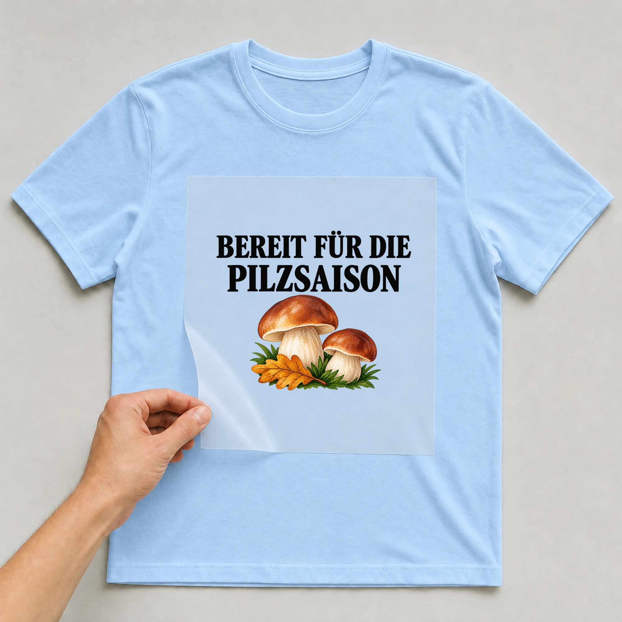 Bügelbild „Bereit für die Pilzsaison“ auf babyblauem T-Shirt, Folie wird aufgelegt