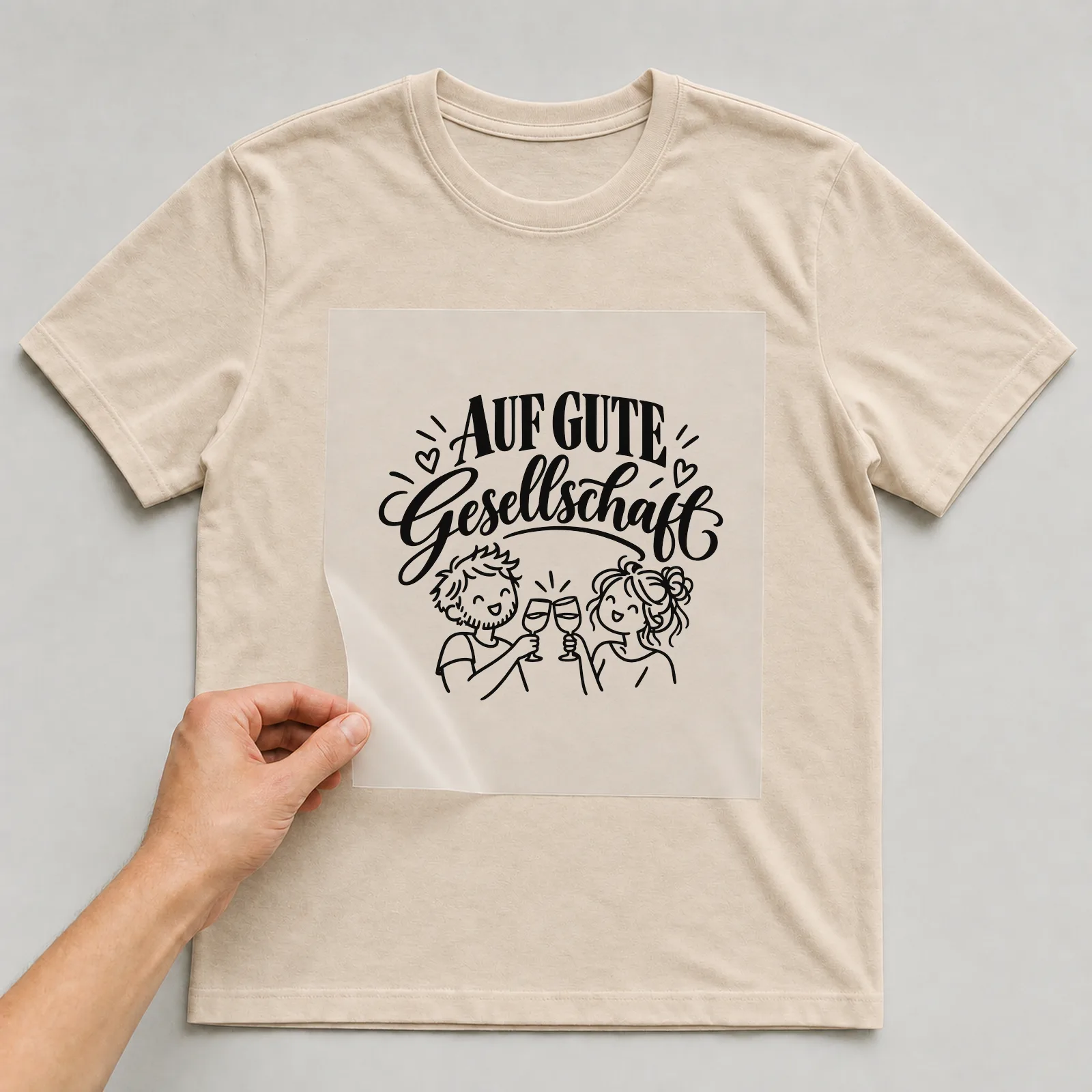 Bügelbild „Auf gute Gesellschaft“ auf beigem T-Shirt, Folie wird aufgelegt