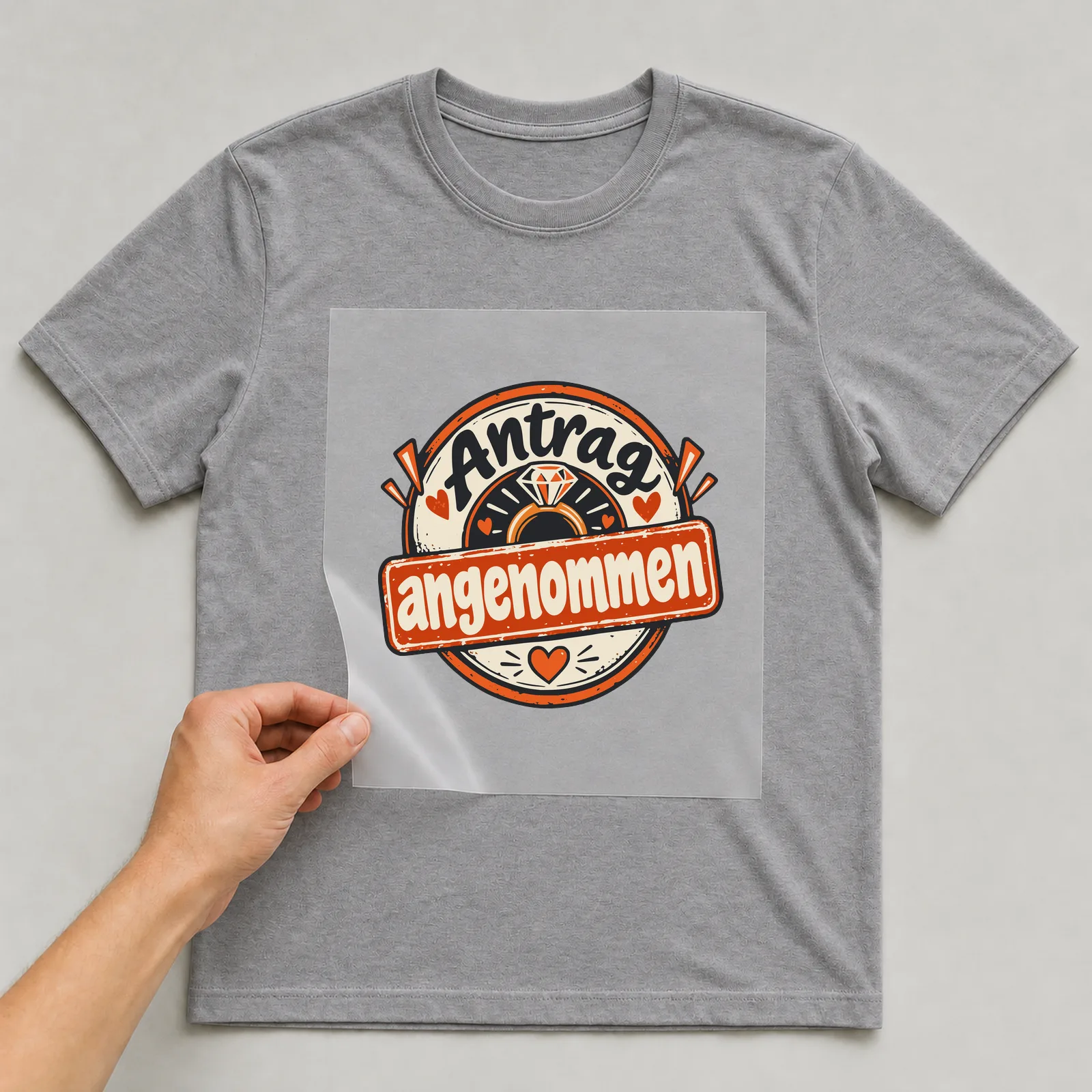 Bügelbild Antrag angenommen auf grauem T-Shirt, Folie wird aufgelegt
