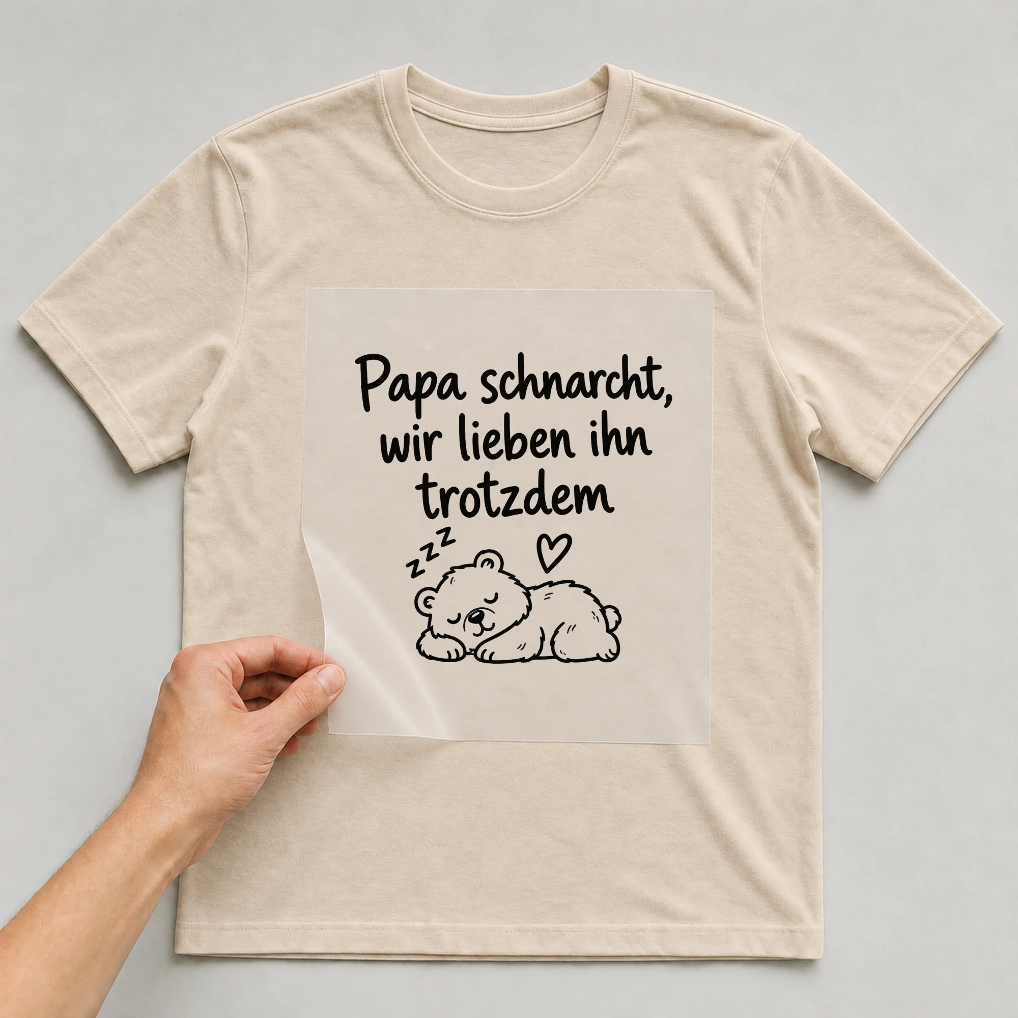 Bügelbild „Papa schnarcht, wir lieben ihn trotzdem“ auf beigem T-Shirt, Folie wird aufgelegt