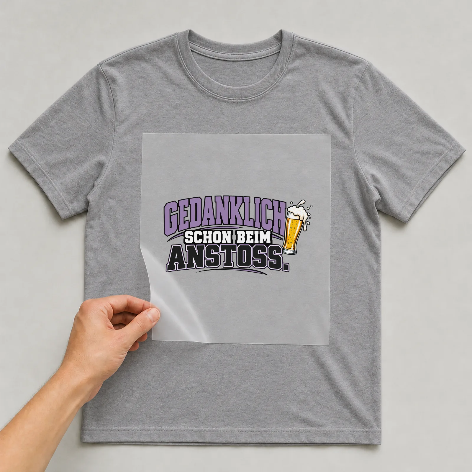 Bügelbild „Gedanklich schon beim Anstoß“ auf grauem T-Shirt, Folie wird aufgelegt