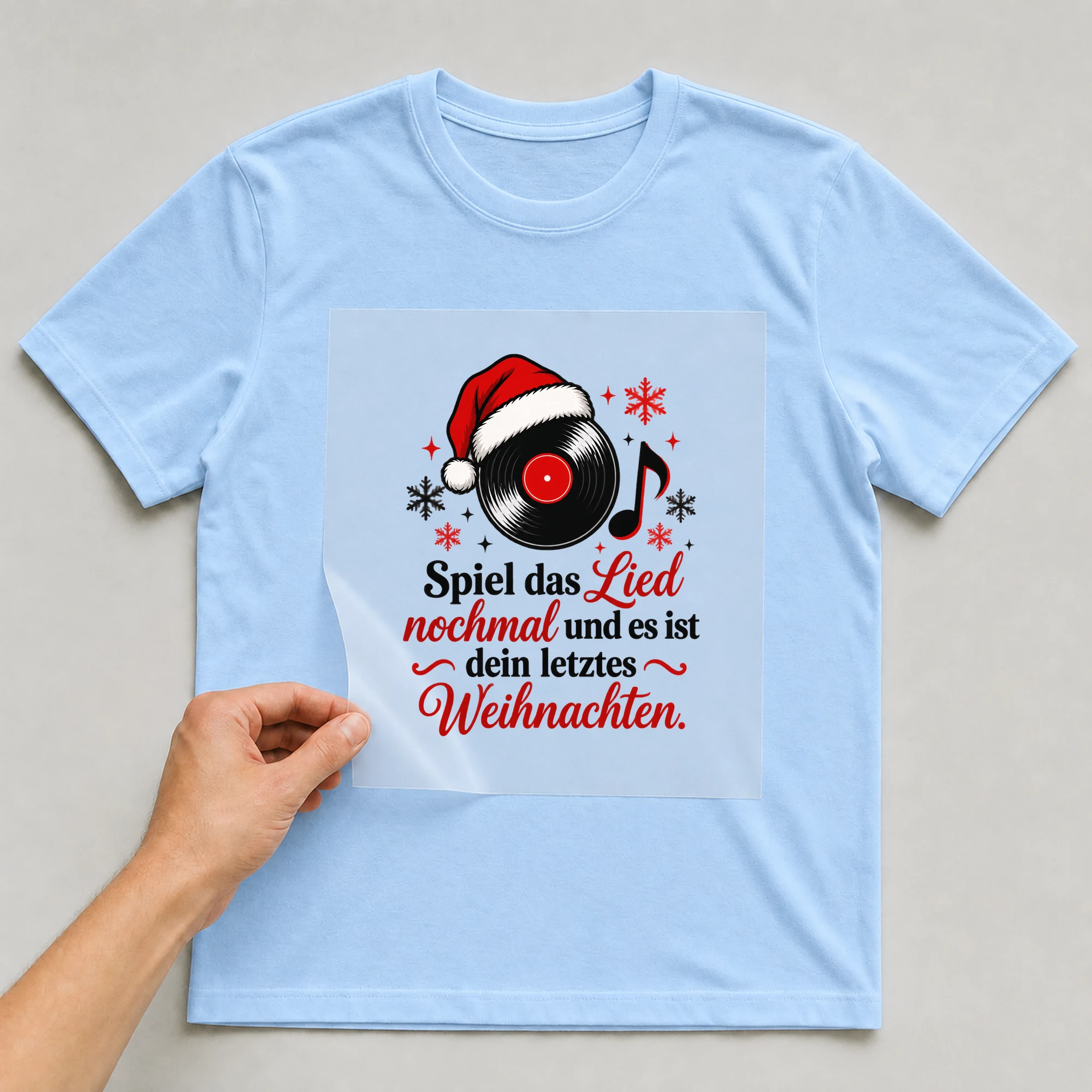 Bügelbild „Spiel das Lied nochmal und es ist dein letztes Weihnachten.“ auf babyblauem T-Shirt, Folie wird aufgelegt