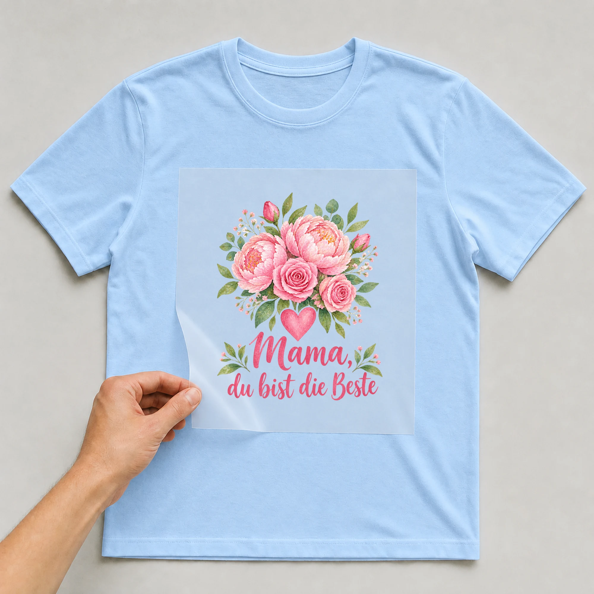 Bügelbild „Mama, du bist die Beste“ auf babyblauem T-Shirt, Folie wird aufgelegt