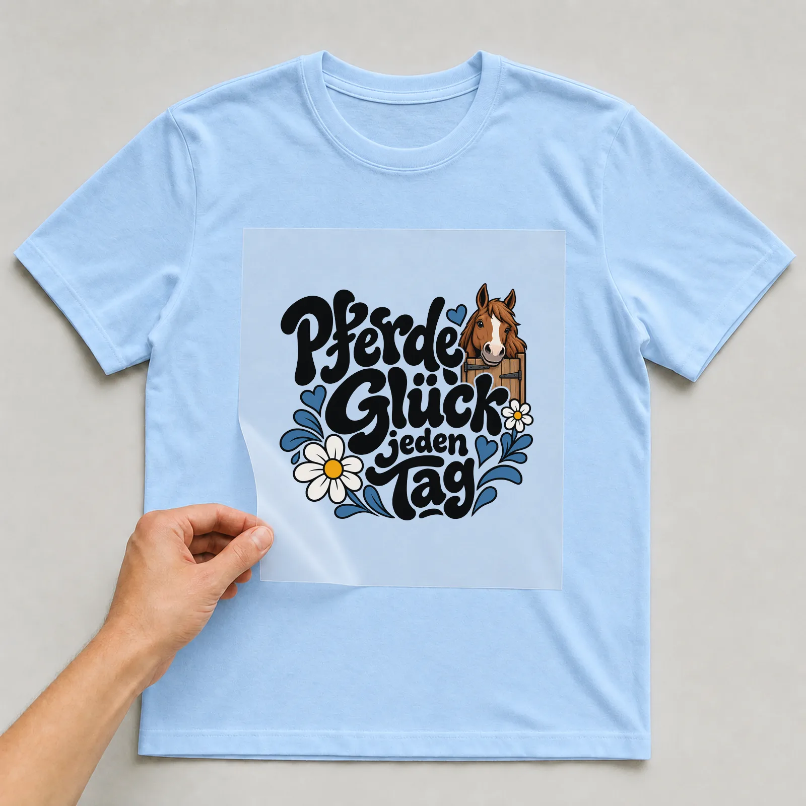 Bügelbild „Pferdeglück jeden Tag“ auf hellblauem T-Shirt, Folie wird aufgelegt