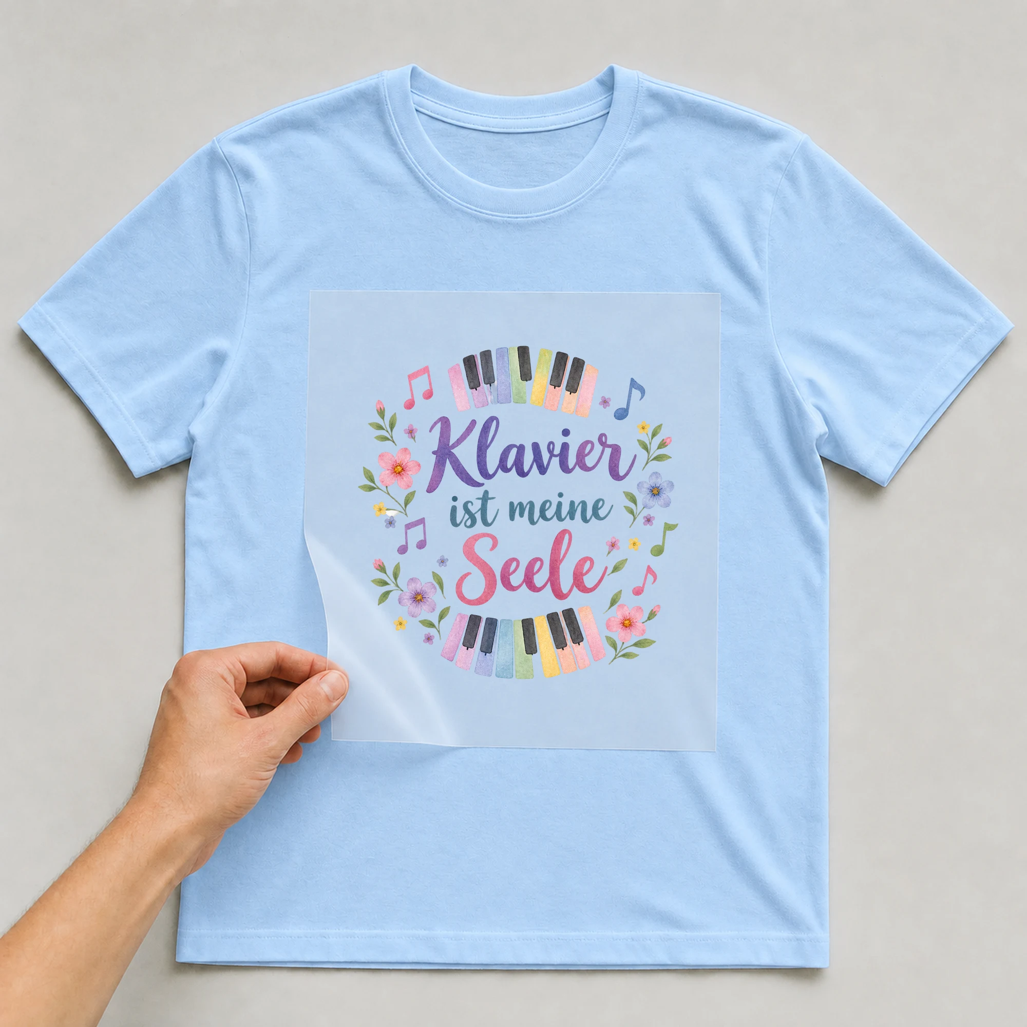Bügelbild „Klavier ist meine Seele“ auf babyblauem T-Shirt, Folie wird aufgelegt