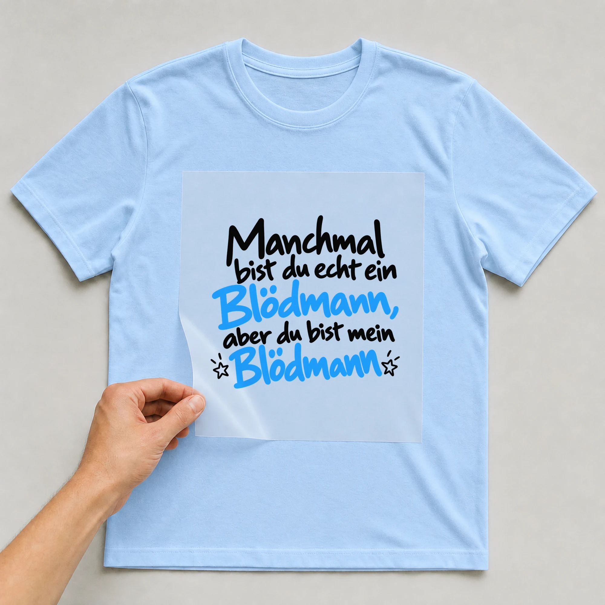 Bügelbild „Manchmal bist du ein Blödmann, aber du bist mein Blödmann“ auf babyblauem T-Shirt, Folie wird aufgelegt