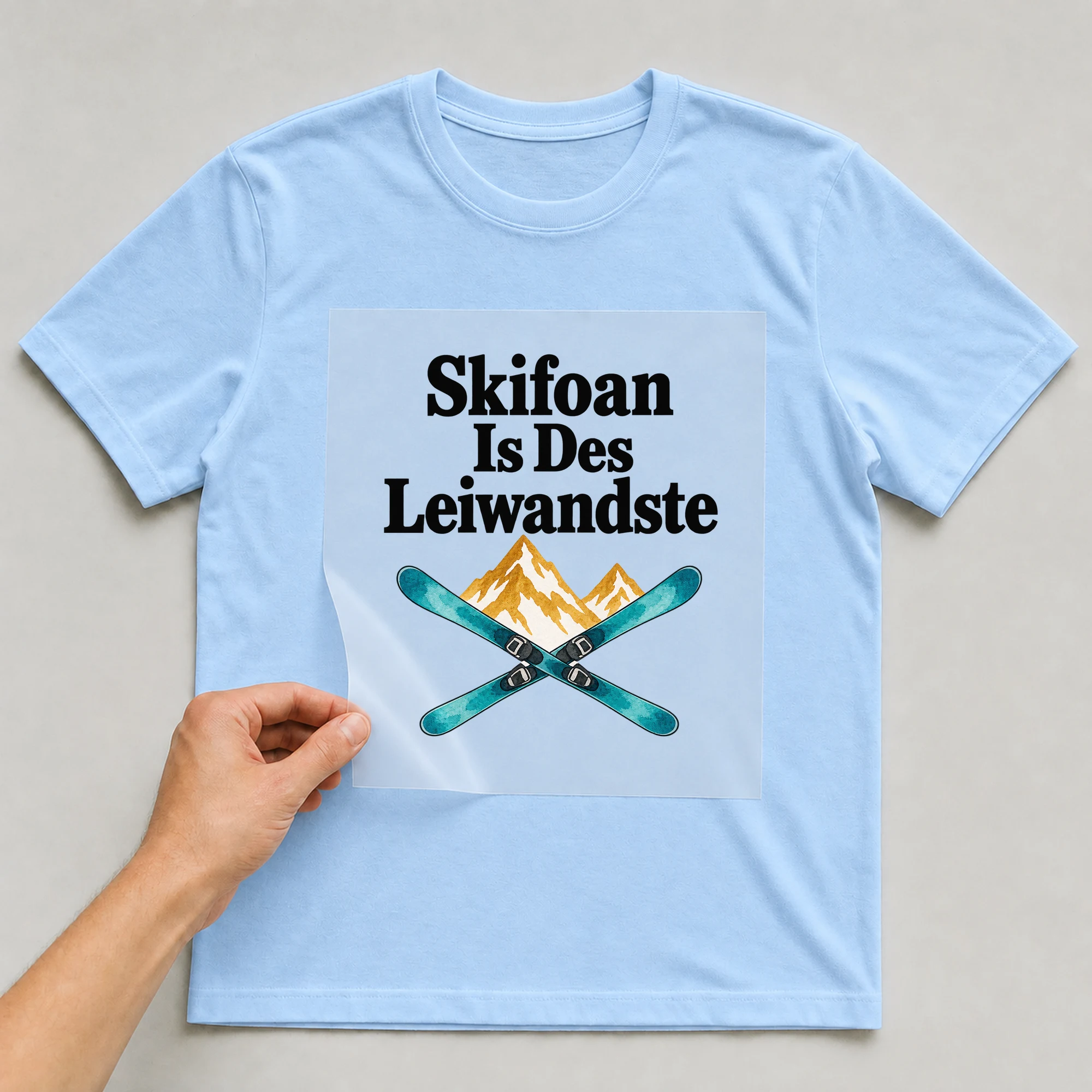 Bügelbild „Skifoan Is Des Leiwandste“ auf babyblauem T-Shirt, Folie wird aufgelegt