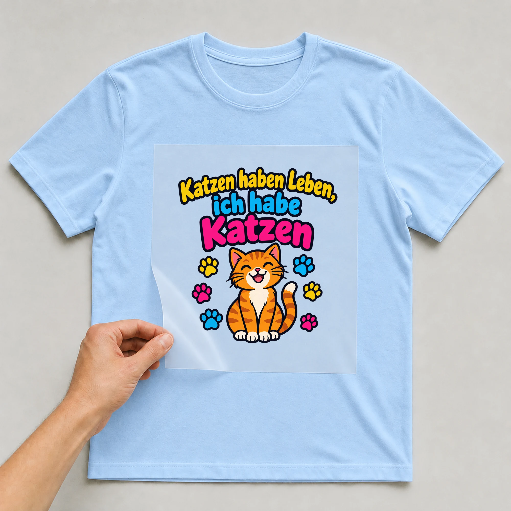 Bügelbild „Katzen haben Leben, ich habe Katzen“ auf babyblauem T-Shirt, Folie wird aufgelegt