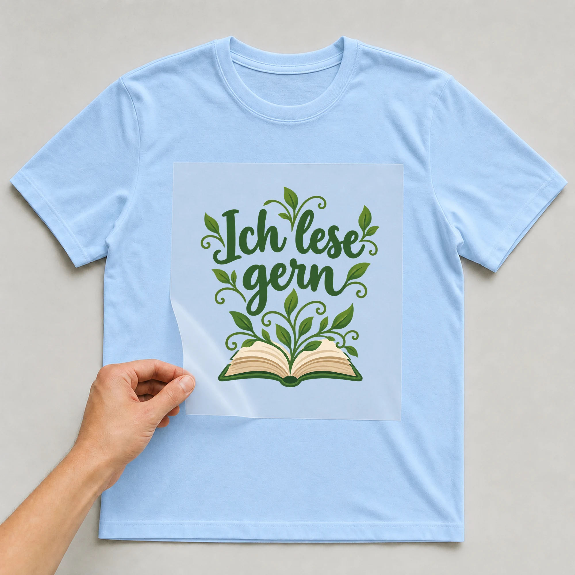 Bügelbild „Ich lese gern“ auf babyblauem T-Shirt, Folie wird aufgelegt