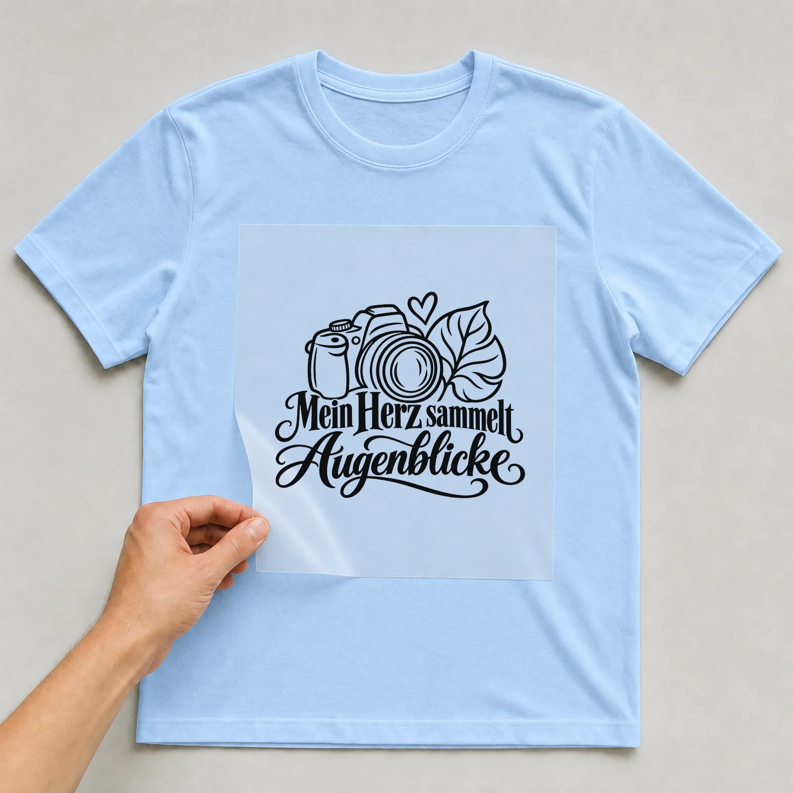 Bügelbild „Mein Herz sammelt Augenblicke“ auf hellblauem T-Shirt, Folie wird aufgelegt