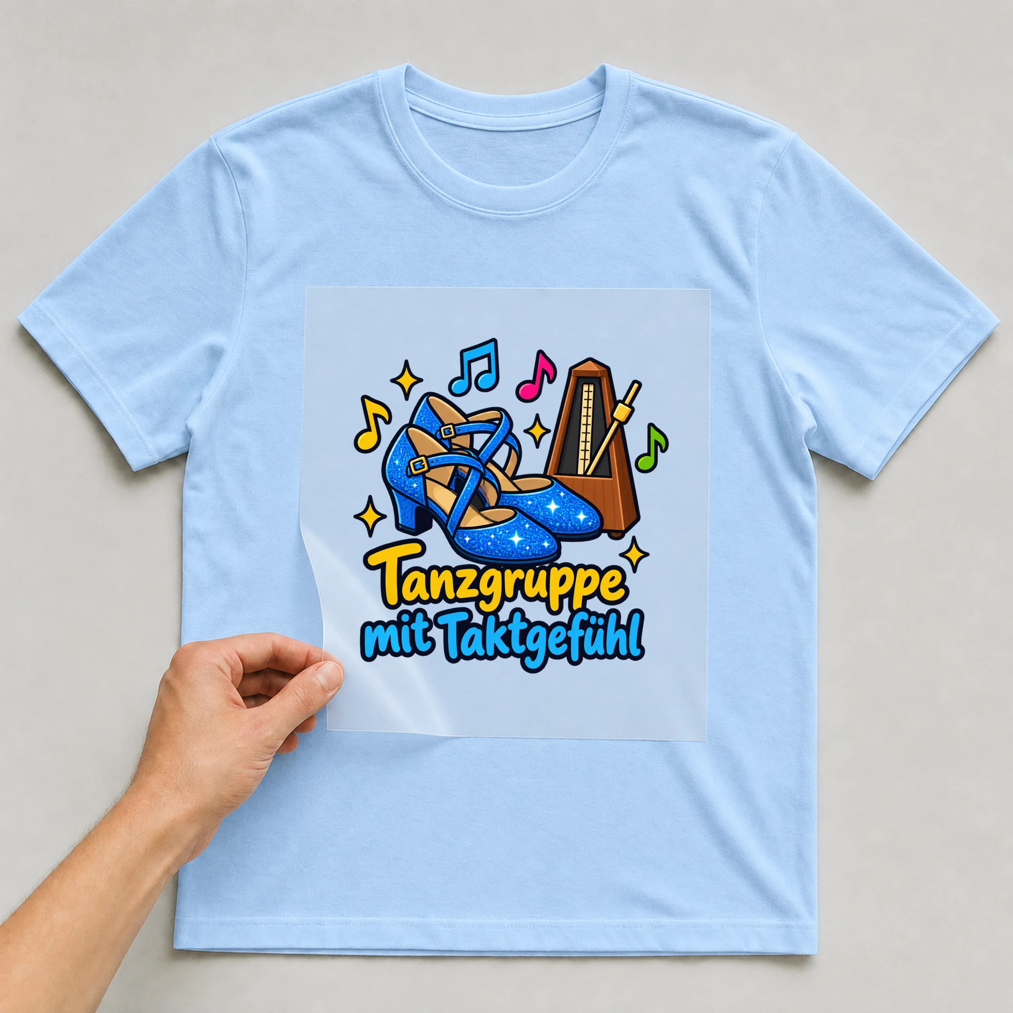 Bügelbild „Tanzgruppe mit Taktgefühl“ auf babyblauem T-Shirt, Folie wird aufgelegt