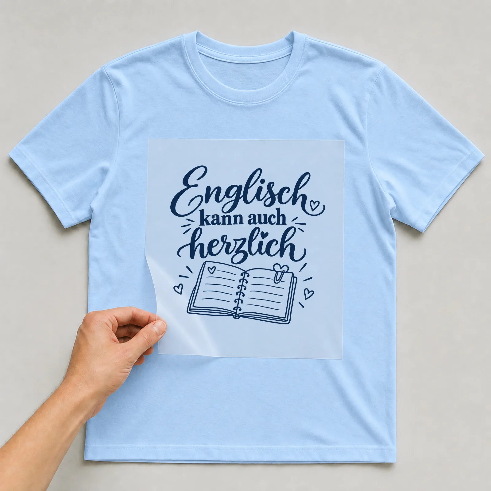 Bügelbild „Englisch kann auch herzlich“ auf hellblauem T-Shirt, Folie wird aufgelegt