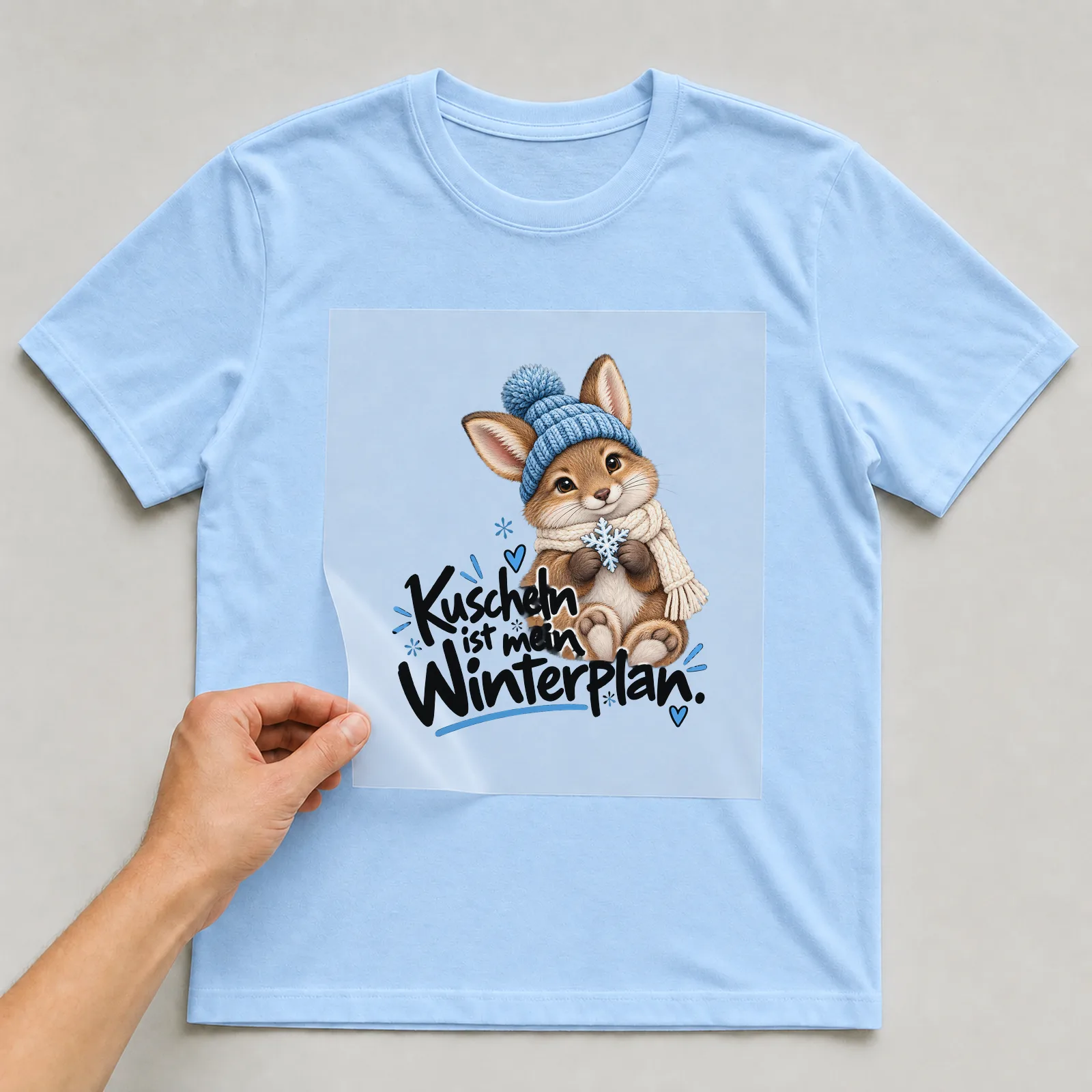 Bügelbild „Kuscheln ist mein Winterplan“ auf hellblauem T-Shirt, Folie wird aufgelegt