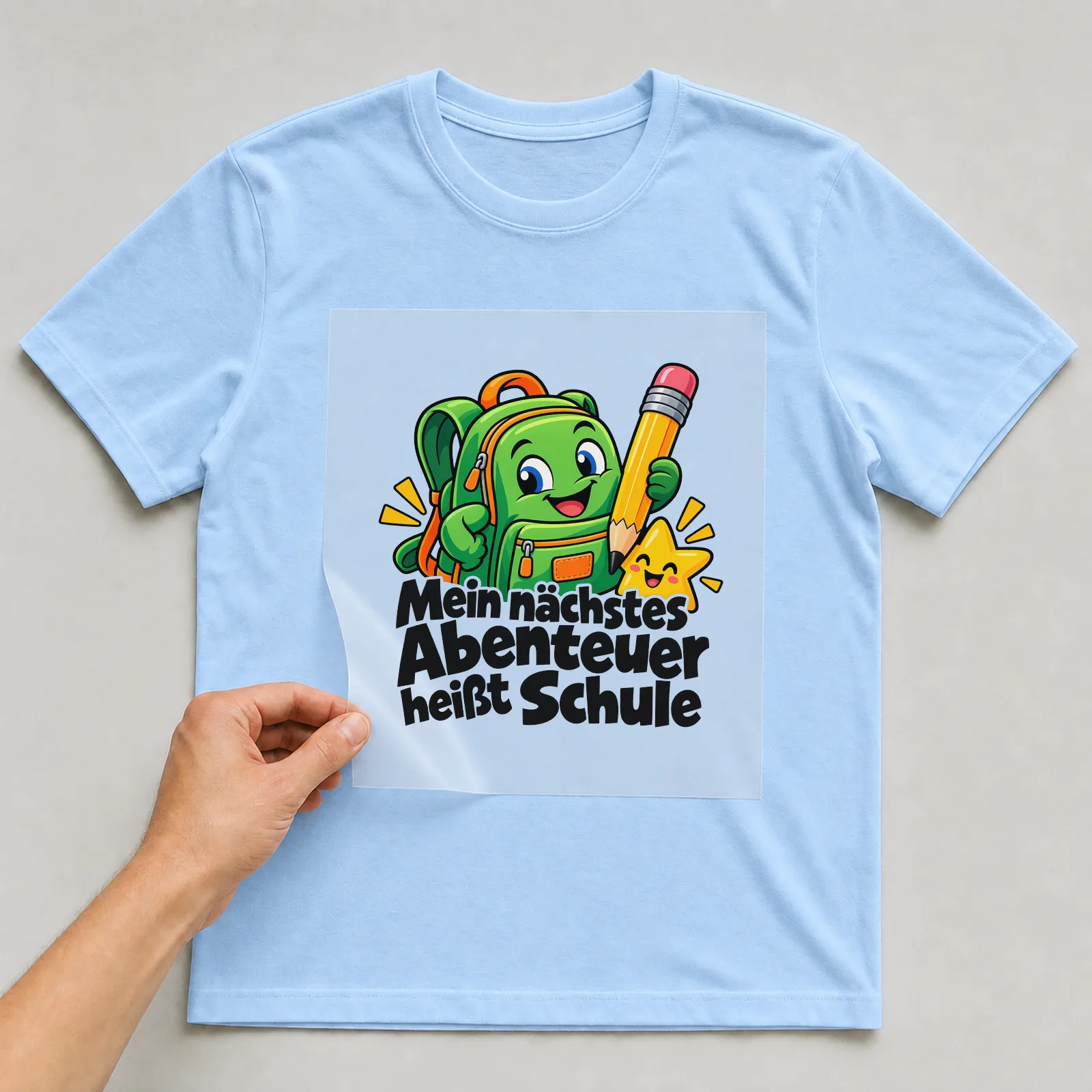 Bügelbild „Mein nächstes Abenteuer heißt Schule“ auf hellblauem T-Shirt, Folie wird aufgelegt