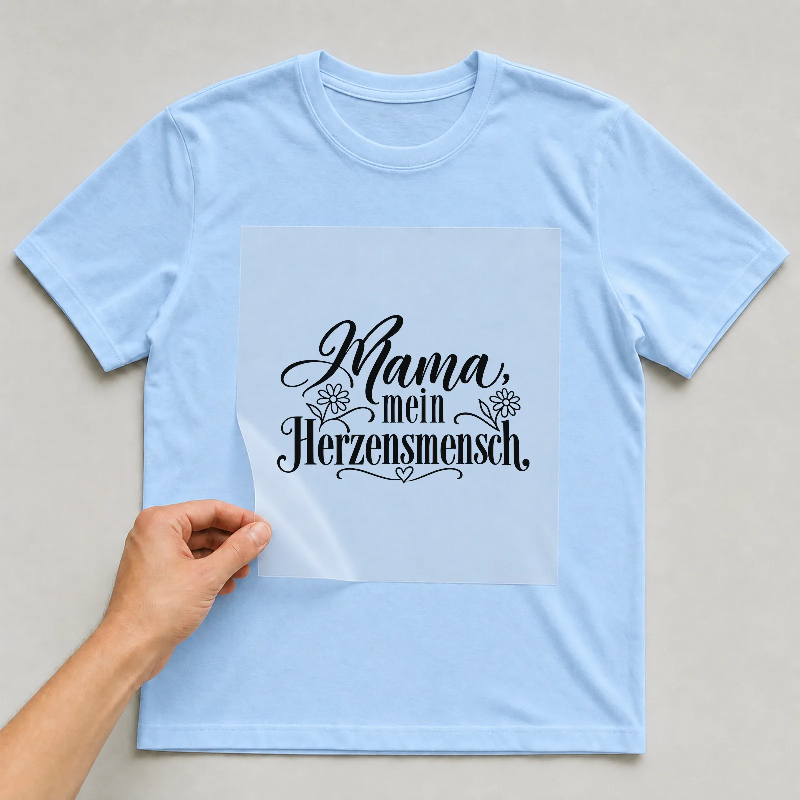 Bügelbild „Mama, mein Herzensmensch“ auf hellblauem T-Shirt, Folie wird aufgelegt