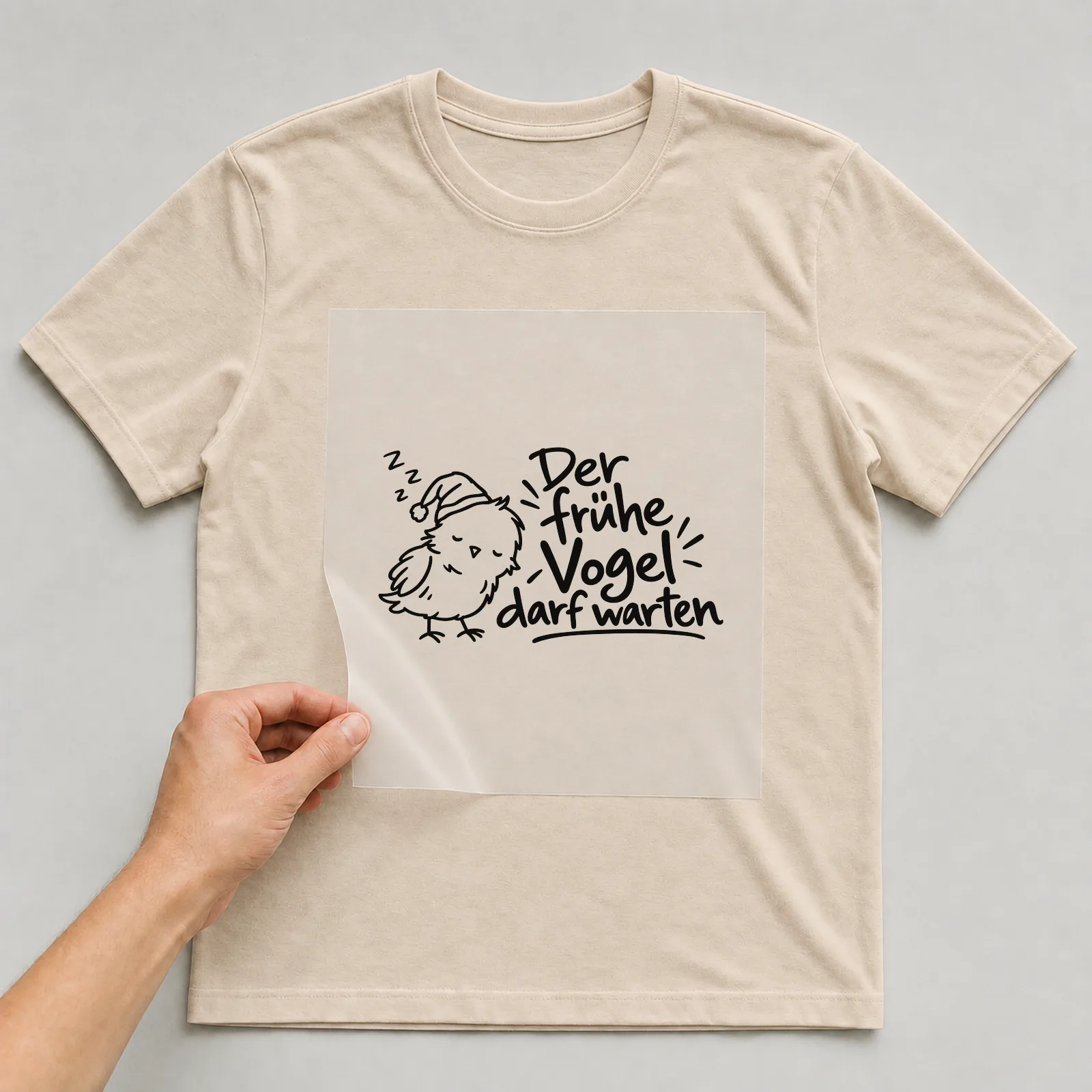 Bügelbild „Der frühe Vogel darf warten“ auf beigem T-Shirt, Folie wird aufgelegt