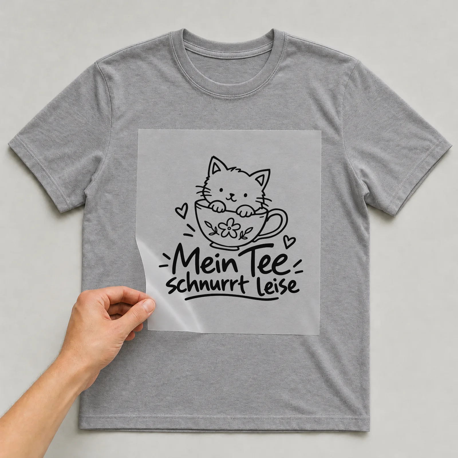 Bügelbild „Mein Tee schnurrt leise“ auf grauem T-Shirt, Folie wird aufgelegt