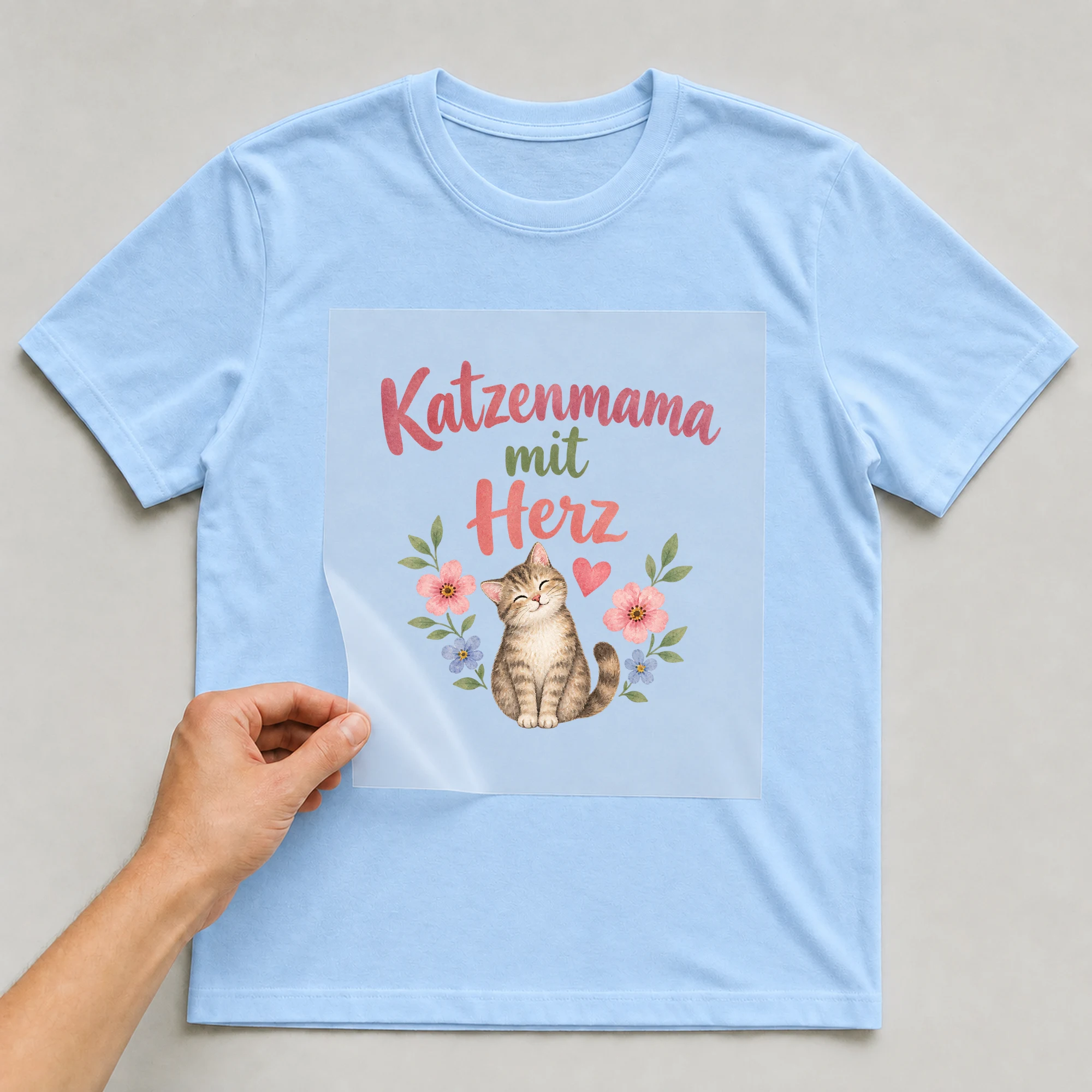 Bügelbild „Katzenmama mit Herz“ auf babyblauem T-Shirt, Folie wird aufgelegt