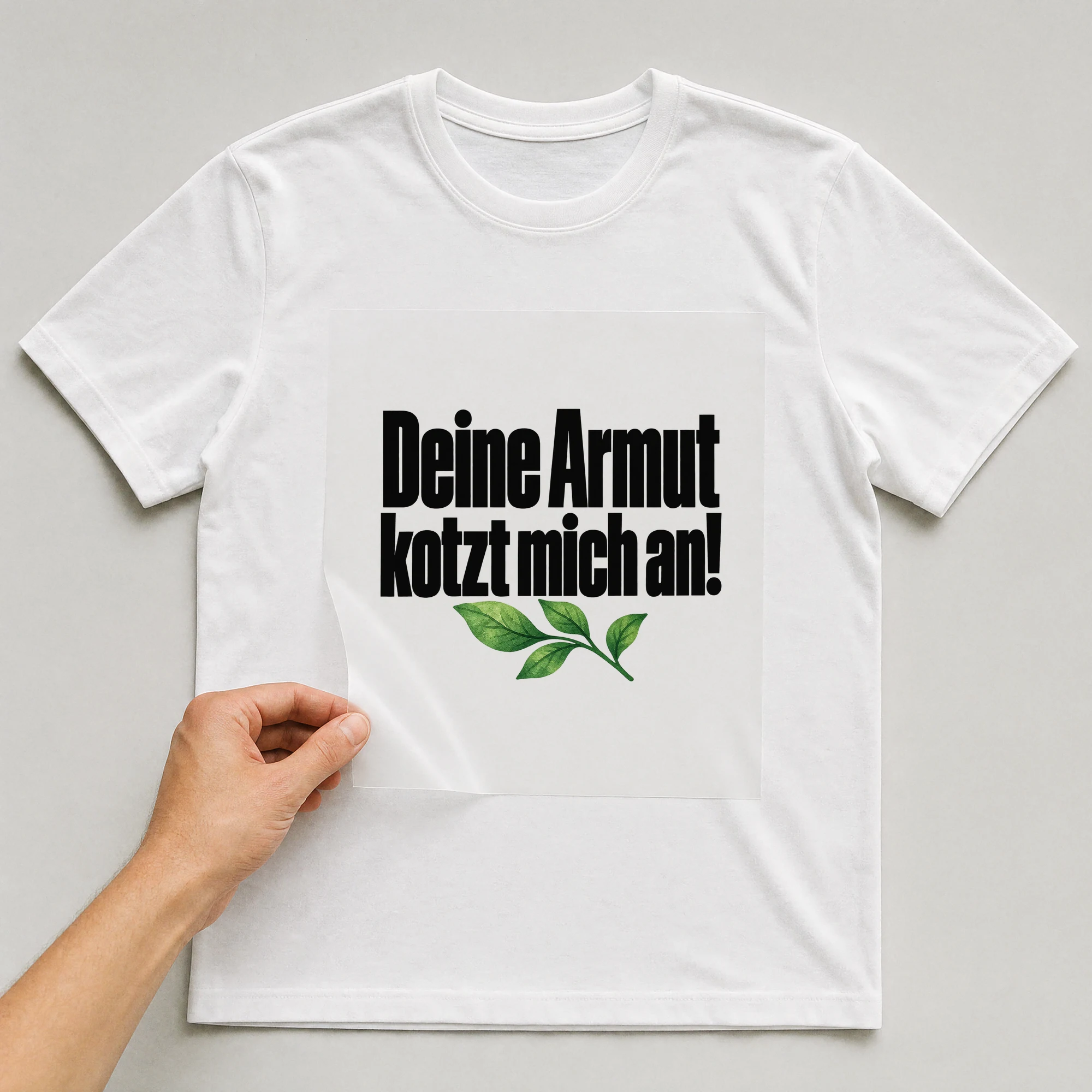 Bügelbild „Deine Armut kotzt mich an!“ auf weißem T-Shirt, Folie wird aufgelegt