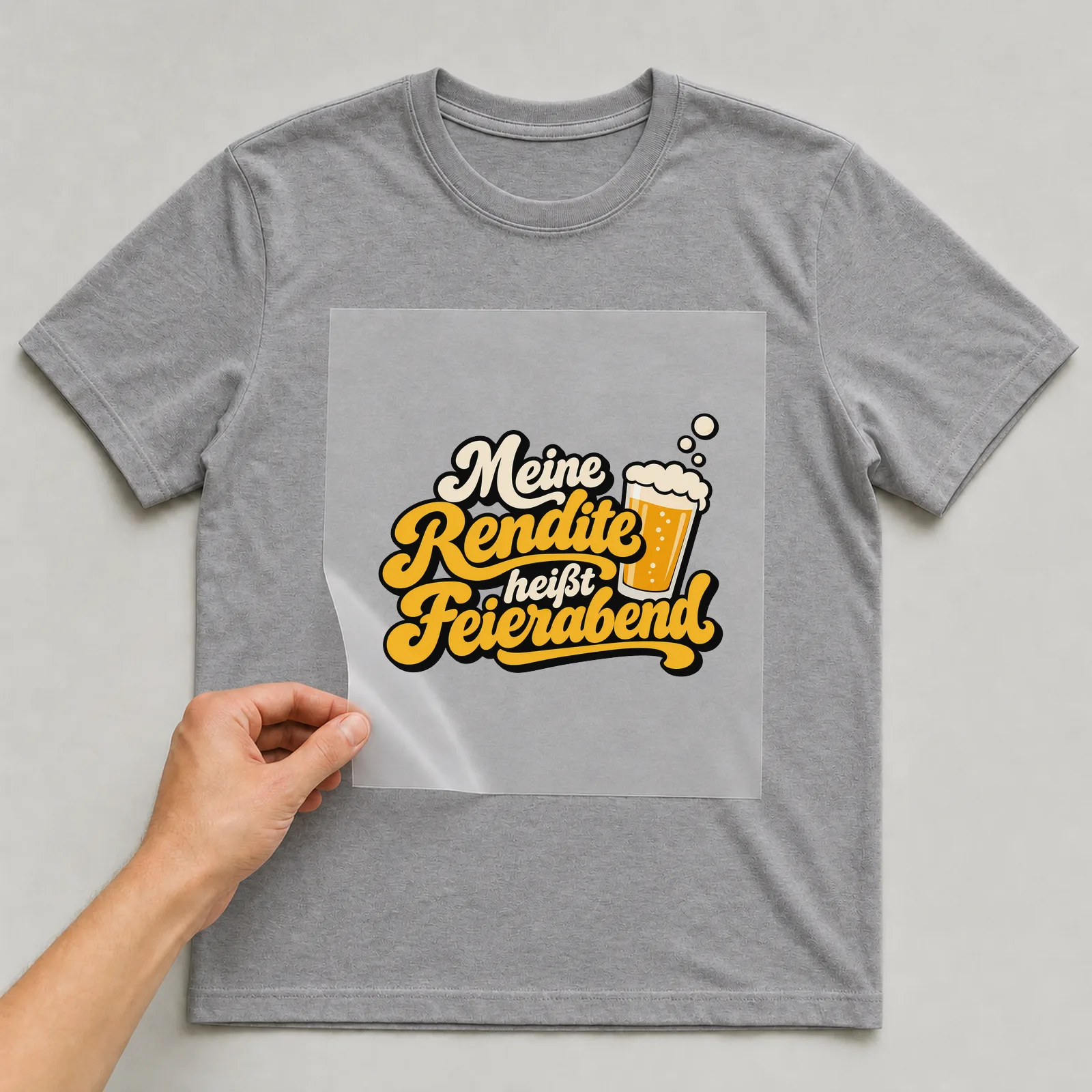 Bügelbild „Meine Rendite heißt Feierabend“ auf grauem T-Shirt, Folie wird aufgelegt