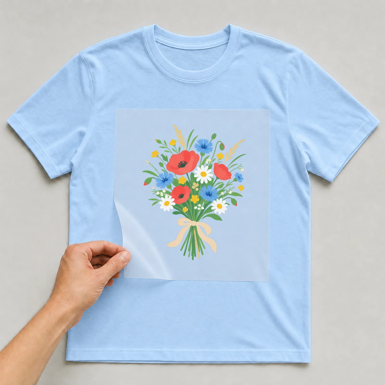 Bügelbild natur wildblumenstrauss auf hellblauem T-Shirt, Folie wird aufgelegt