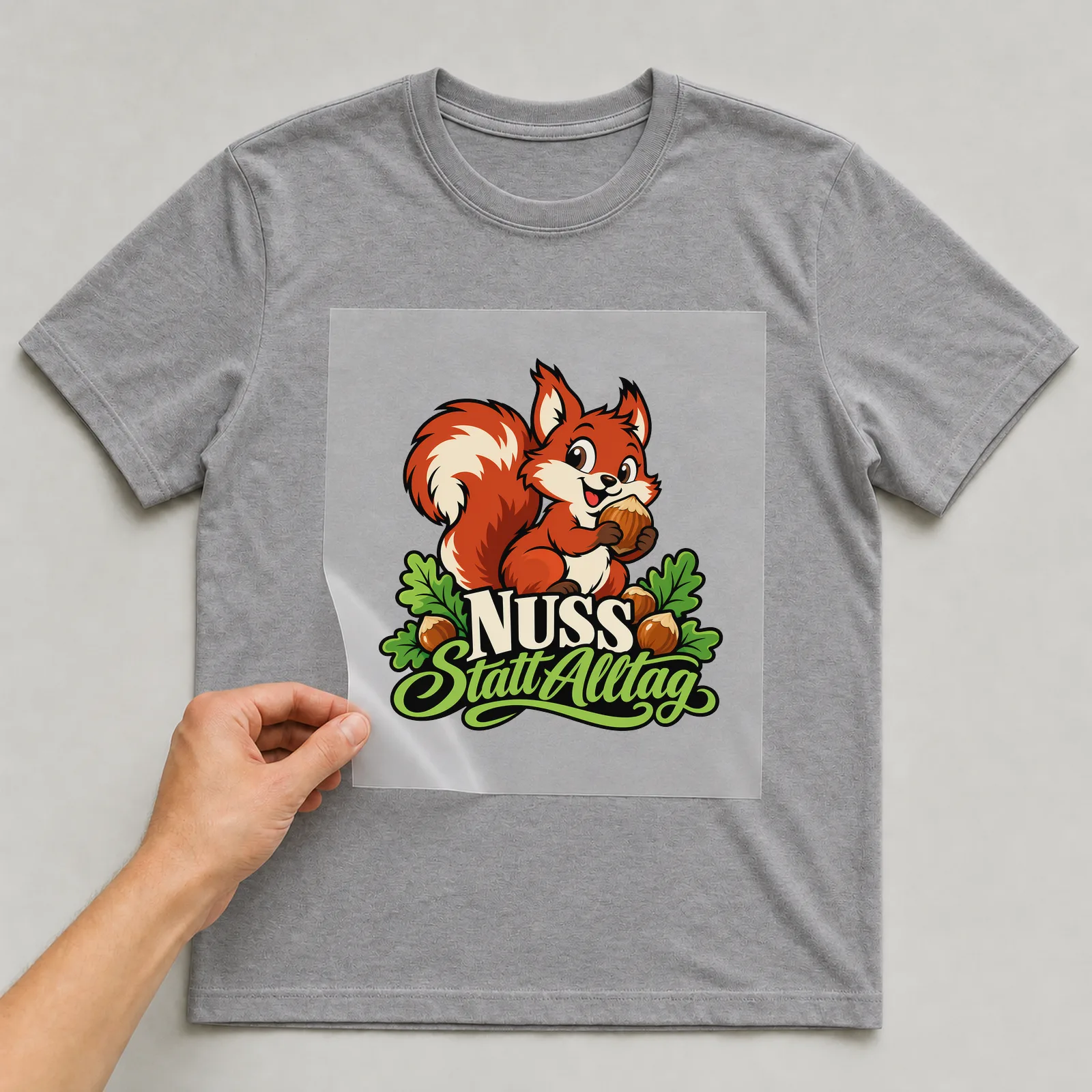 Bügelbild „Nuss statt Alltag“ auf grauem T-Shirt, Folie wird aufgelegt