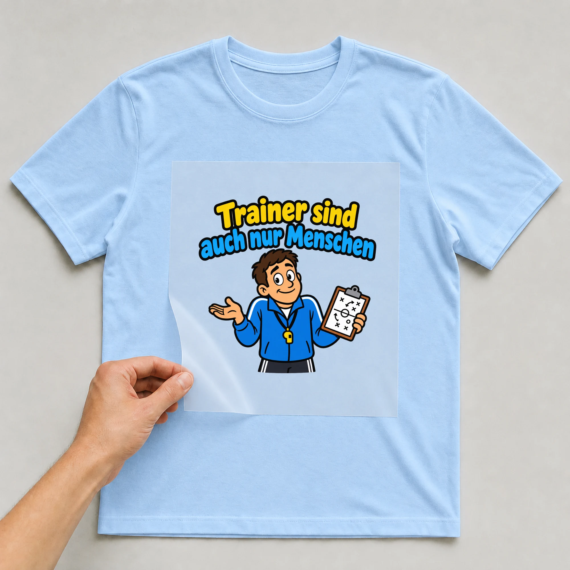 Bügelbild „Trainer sind auch nur Menschen“ auf babyblauem T-Shirt, Folie wird aufgelegt