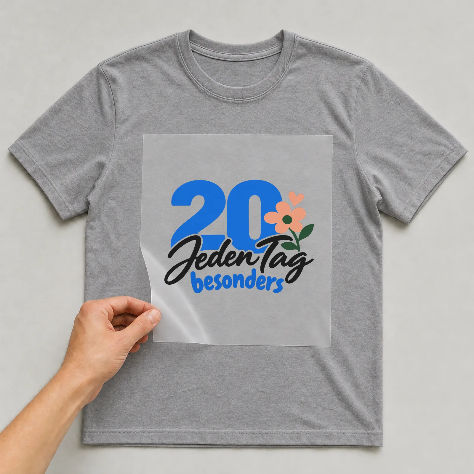 Bügelbild „20 · Jeden Tag besonders“ auf grauem T-Shirt, Folie wird aufgelegt
