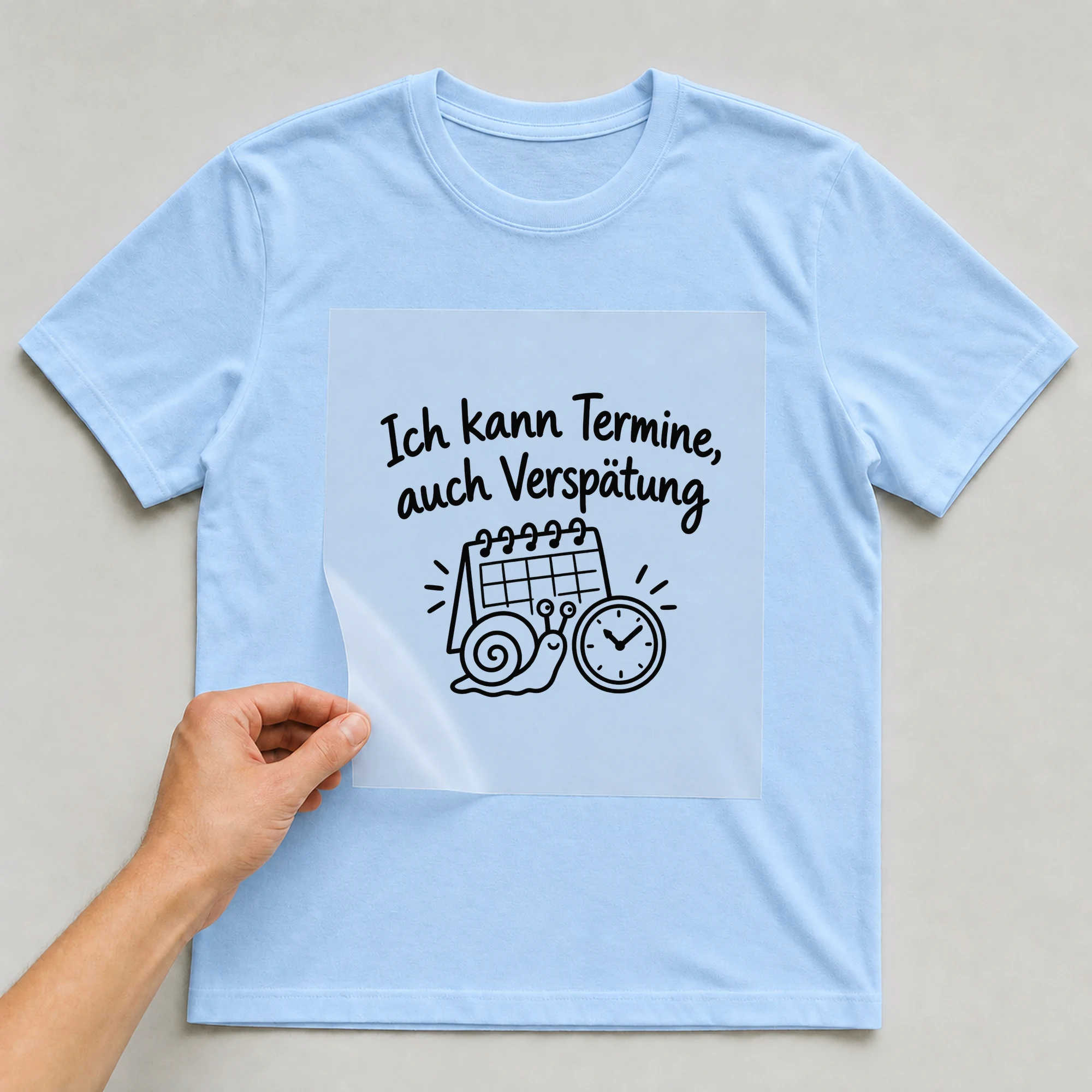 Bügelbild „Ich kann Termine, auch Verspätung“ auf babyblauem T-Shirt, Folie wird aufgelegt