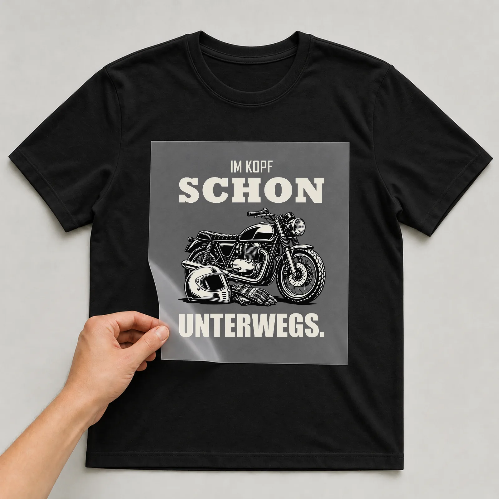 Bügelbild „Im Kopf schon unterwegs“ auf schwarzem T-Shirt, Folie wird aufgelegt