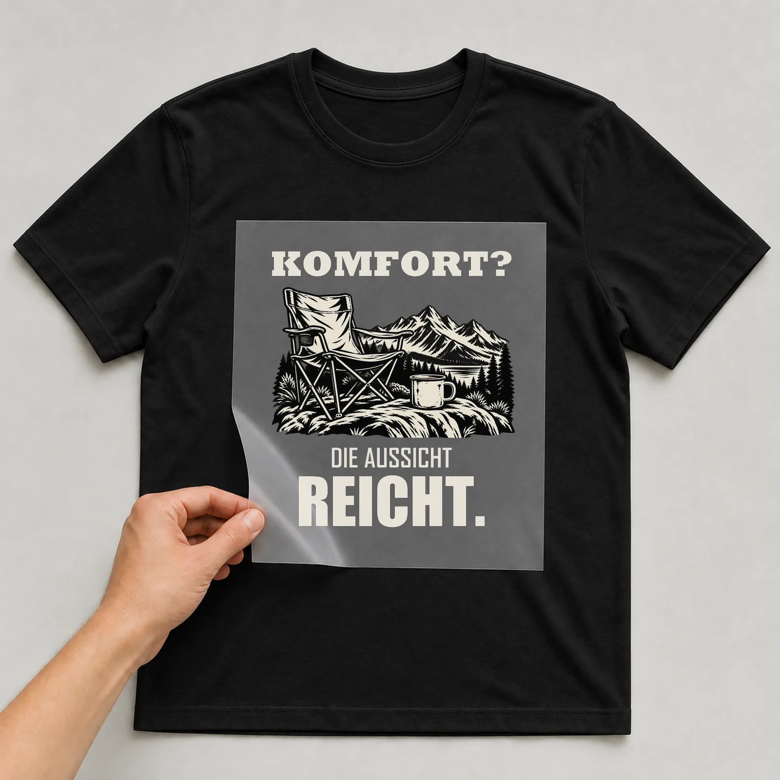 Bügelbild „Komfort? Die Aussicht reicht.“ auf schwarzem T-Shirt, Folie wird aufgelegt