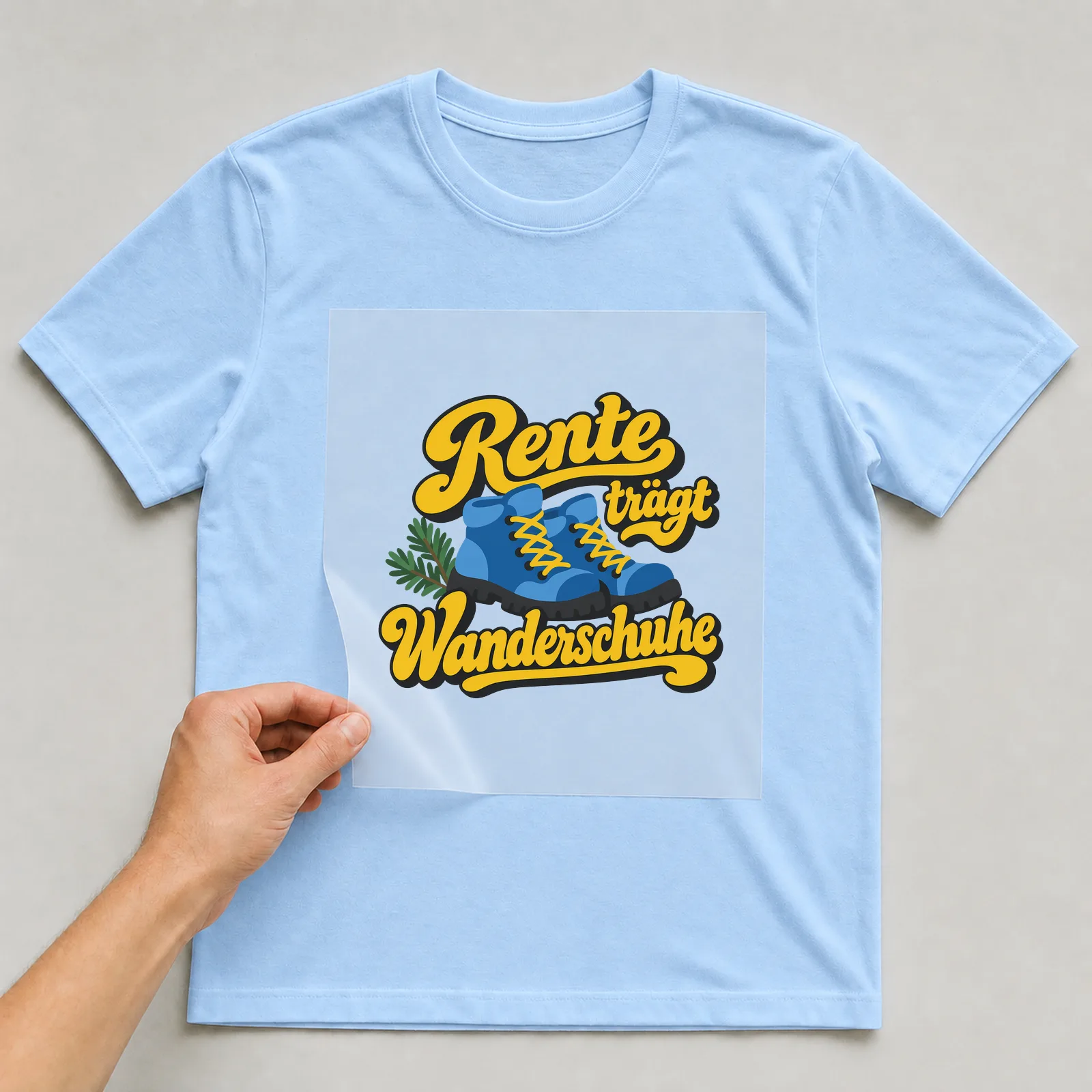 Bügelbild „Rente trägt Wanderschuhe“ auf hellblauem T-Shirt, Folie wird aufgelegt
