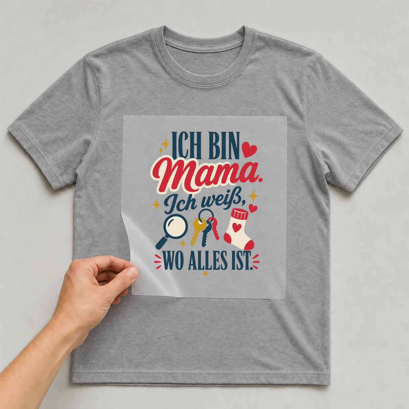 Bügelbild Ich bin Mama. Ich weiß, wo alles ist. auf grauem T-Shirt, Folie wird aufgelegt