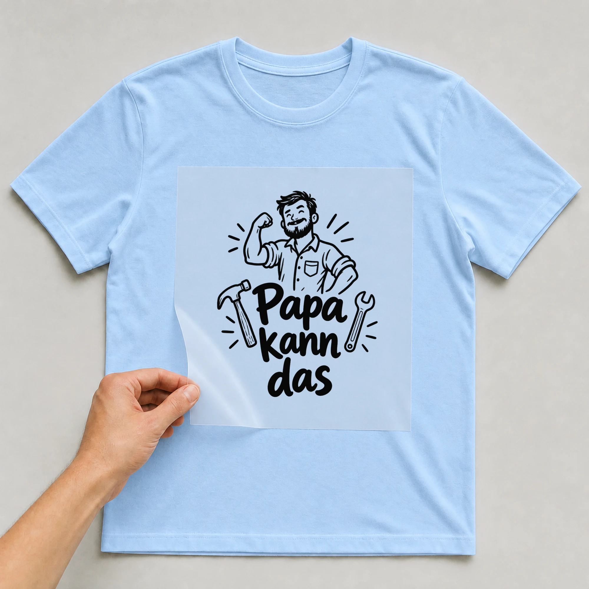 Bügelbild „Papa kann das“ auf babyblauem T-Shirt, Folie wird aufgelegt