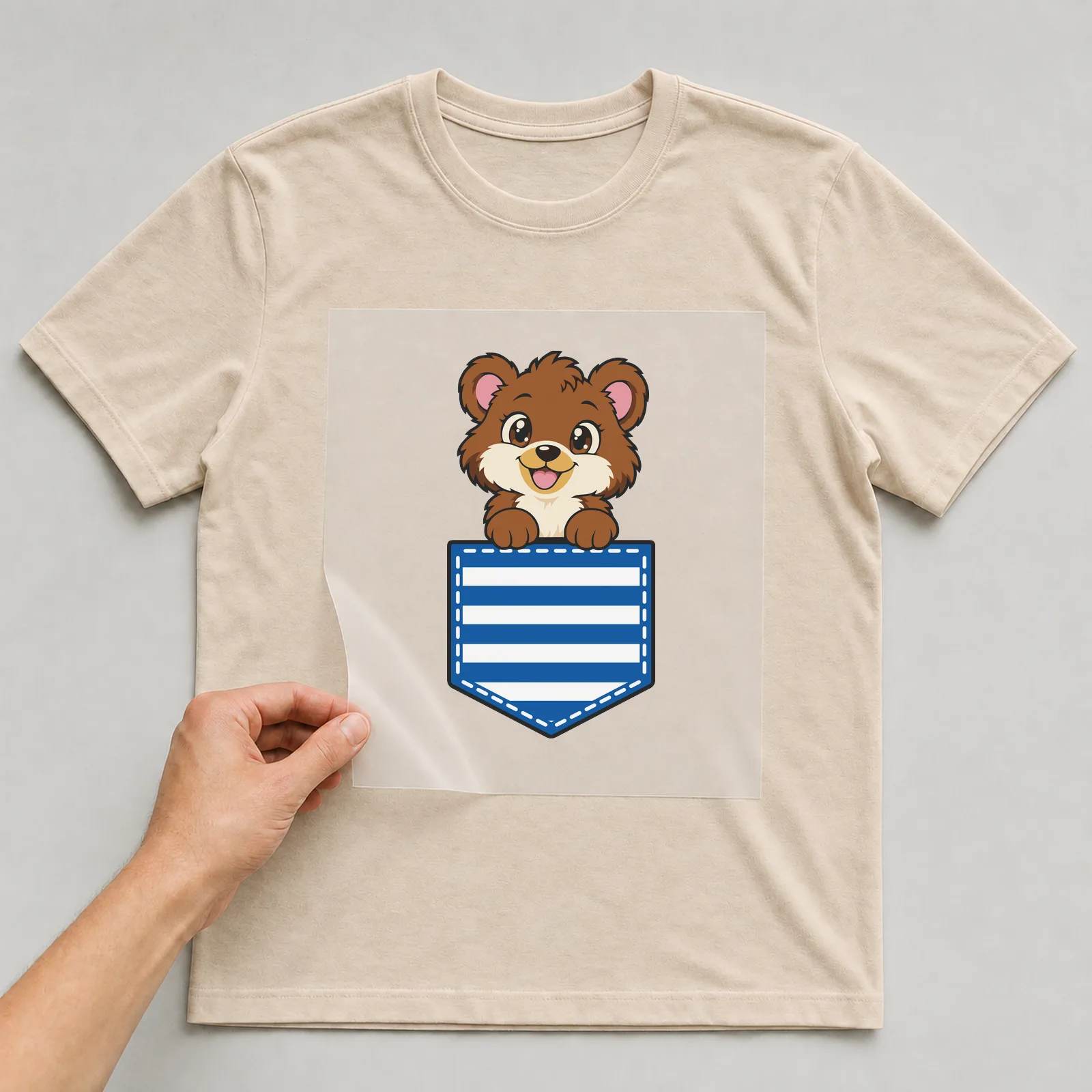 Bügelbild Brusttasche Bär auf beigem T-Shirt, Folie wird aufgelegt