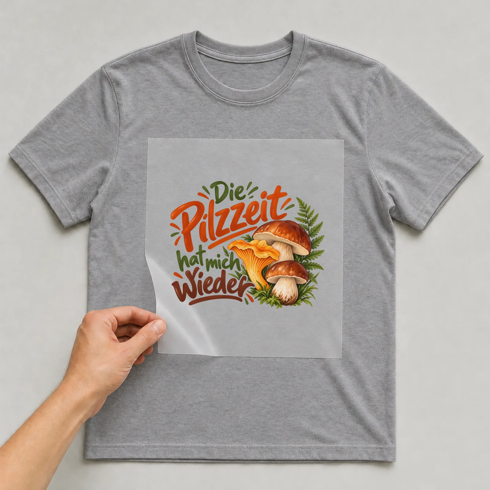 Bügelbild „Die Pilzzeit hat mich wieder“ auf grauem T-Shirt, Folie wird aufgelegt