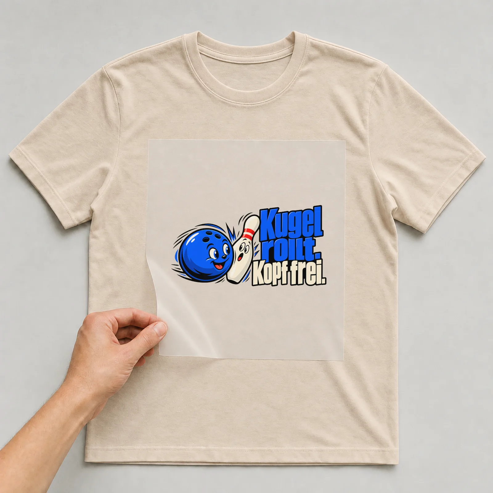 Bügelbild „Kugel rollt. Kopf frei.“ auf beigem T-Shirt, Folie wird aufgelegt