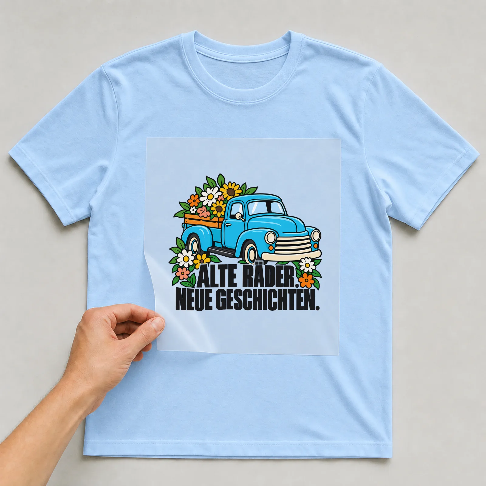 Bügelbild „Alte Räder neue Geschichten“ auf hellblauem T-Shirt, Folie wird aufgelegt