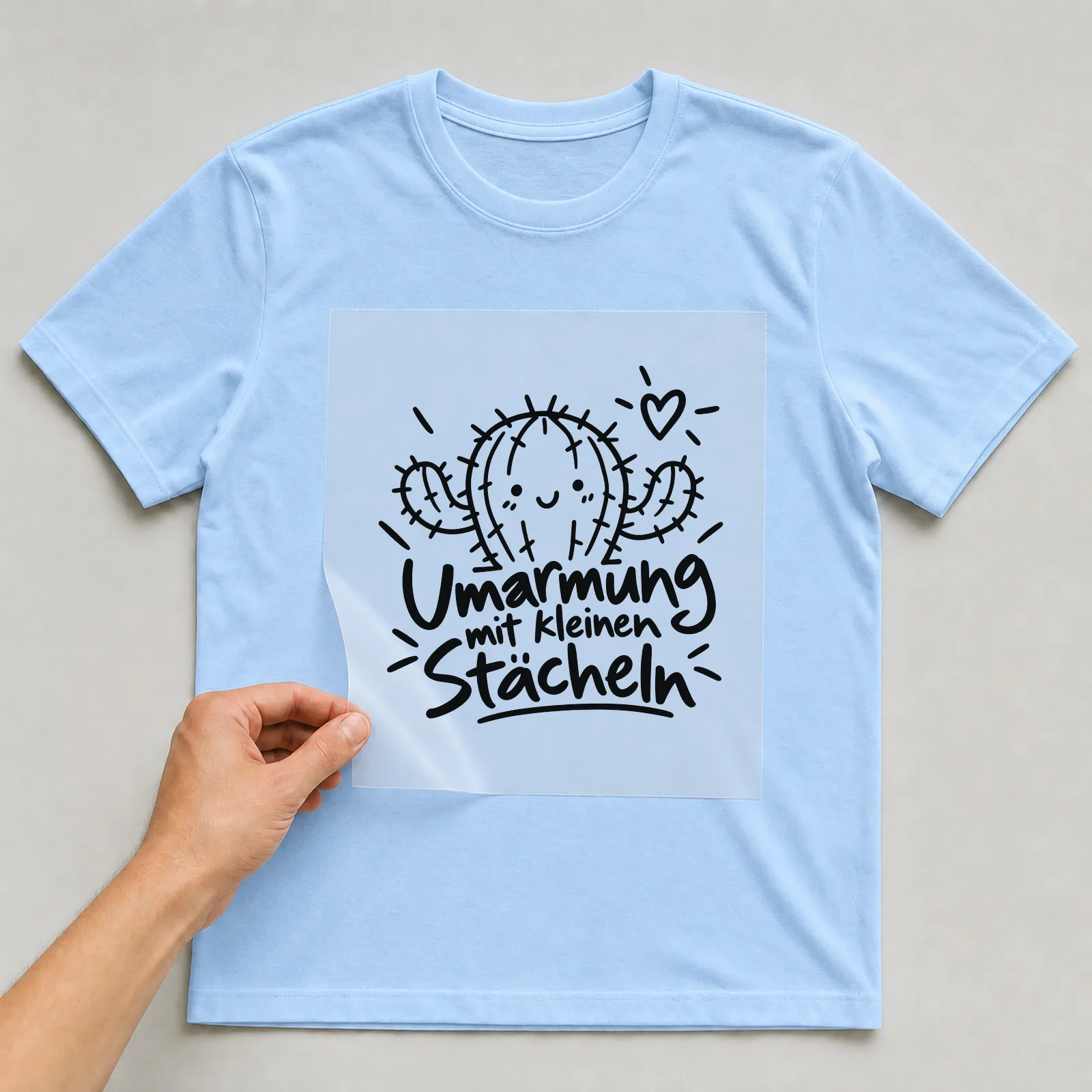Bügelbild „Umarmung mit kleinen Stacheln“ auf hellblauem T-Shirt, Folie wird aufgelegt