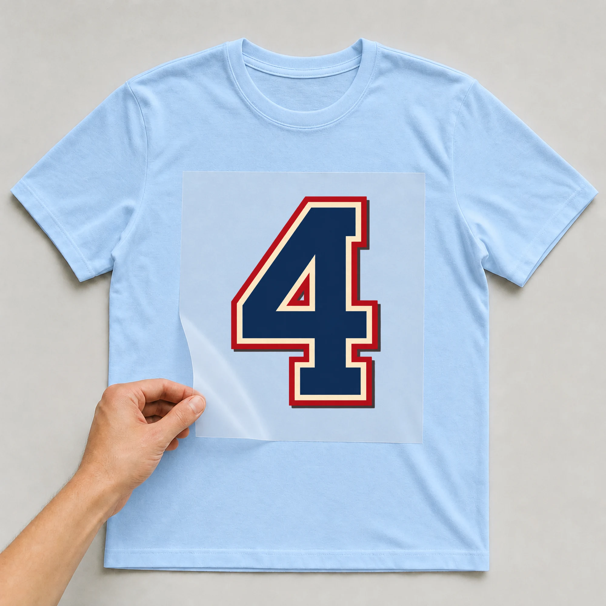 Bügelbild „Zahl 4 im Retro-College-Stil“ auf babyblauem T-Shirt, Folie wird aufgelegt