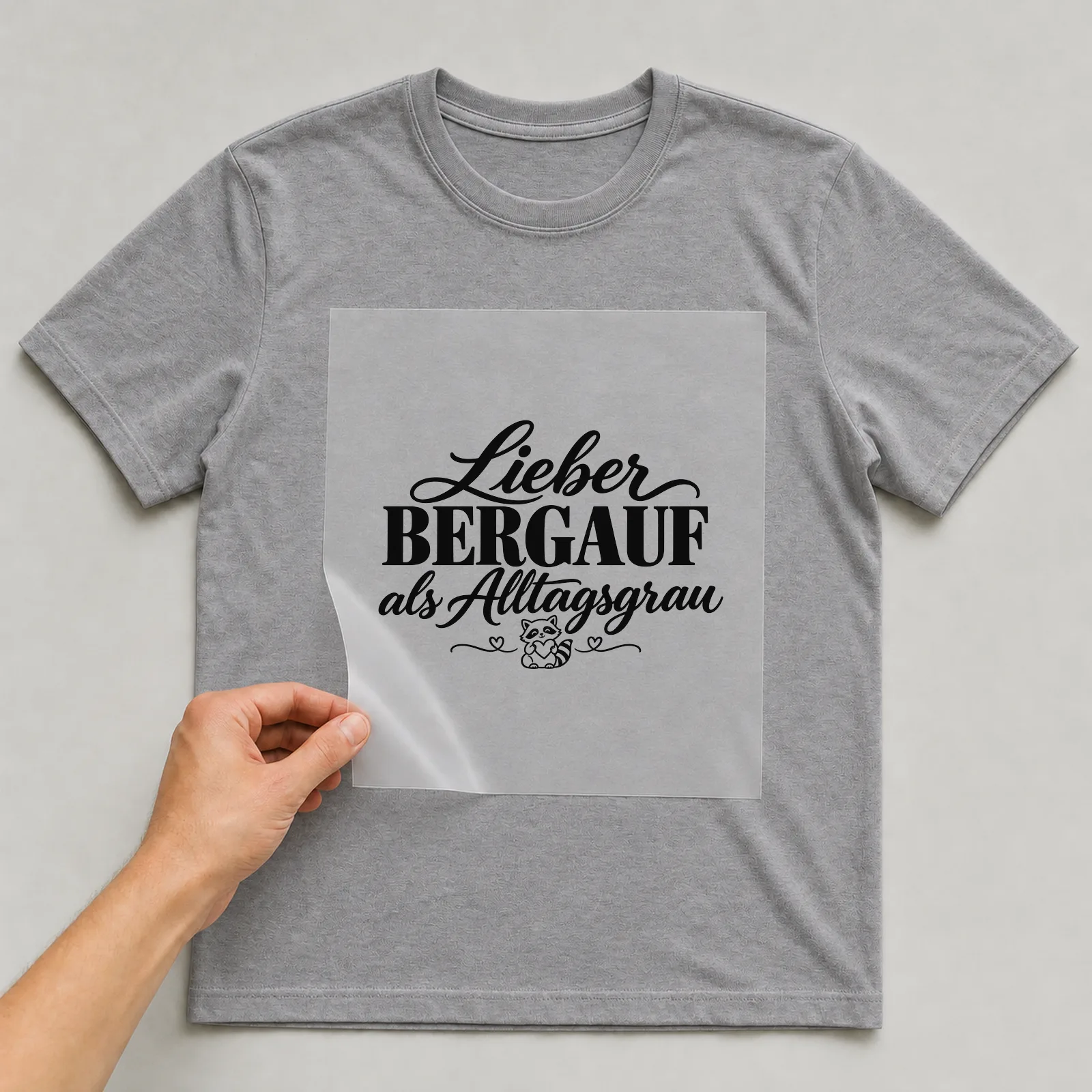 Bügelbild „Lieber bergauf als Alltagsgrau“ auf grauem T-Shirt, Folie wird aufgelegt
