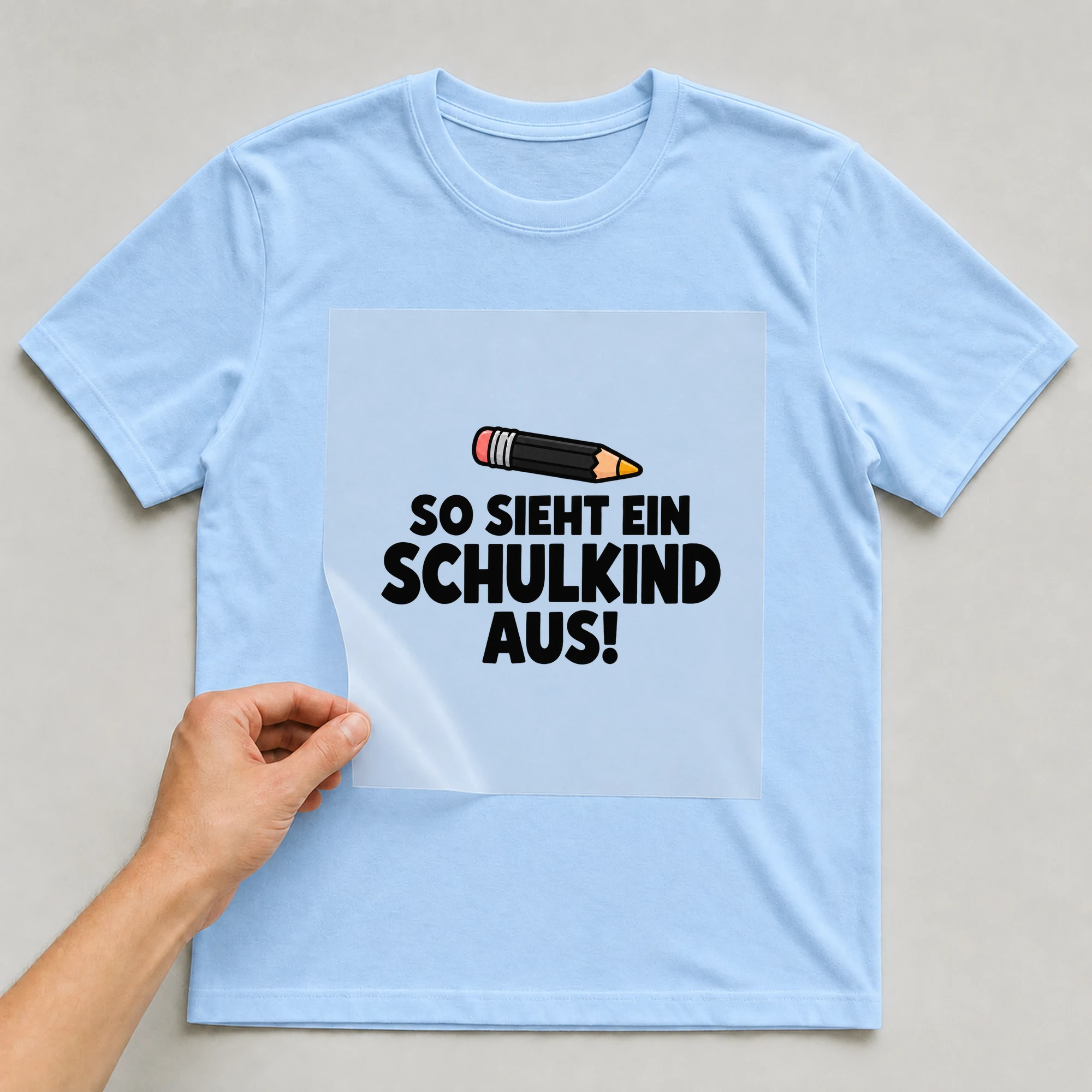 Bügelbild „So sieht ein Schulkind aus!“ auf babyblauem T-Shirt, Folie wird aufgelegt