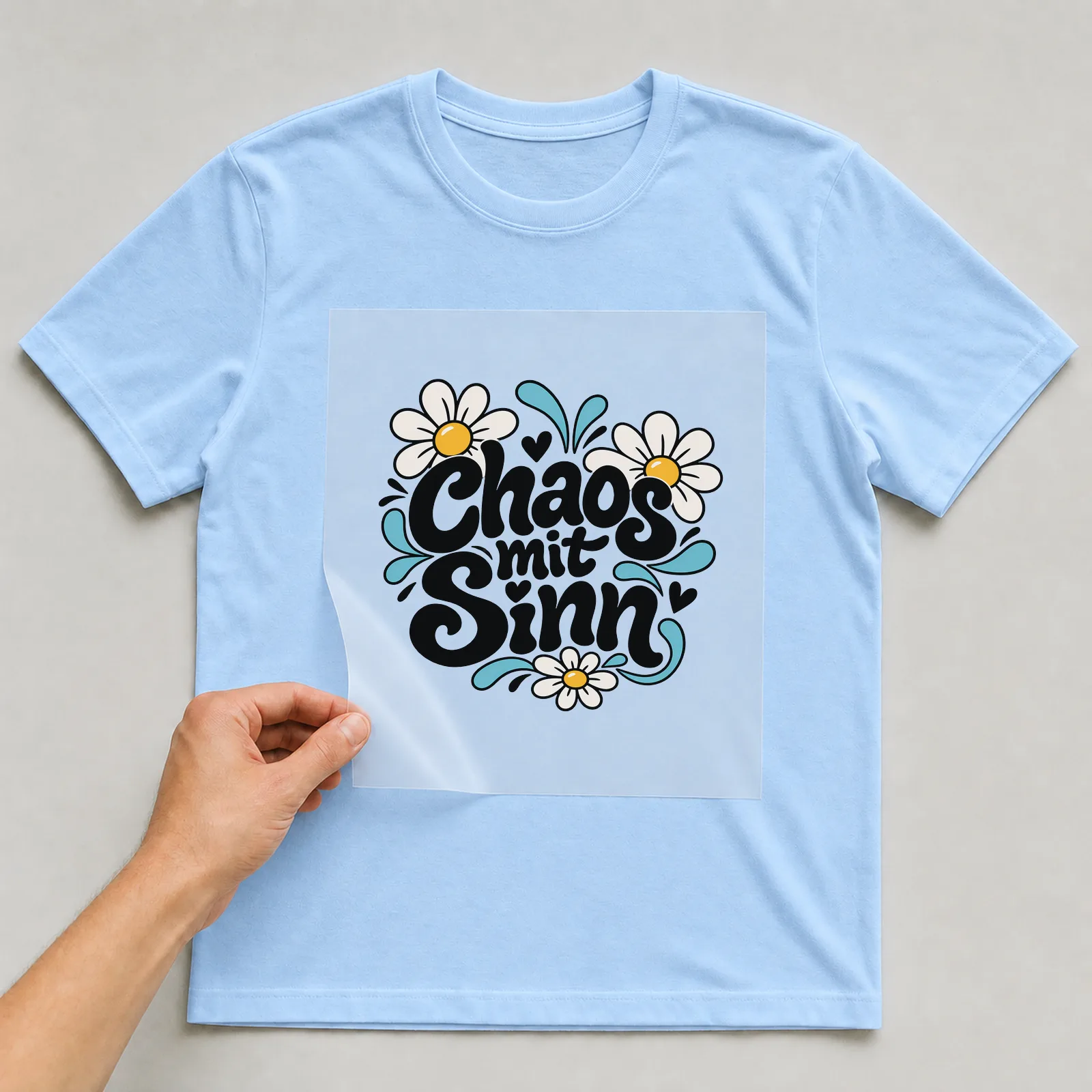 Bügelbild „Chaos mit Sinn“ auf hellblauem T-Shirt, Folie wird aufgelegt