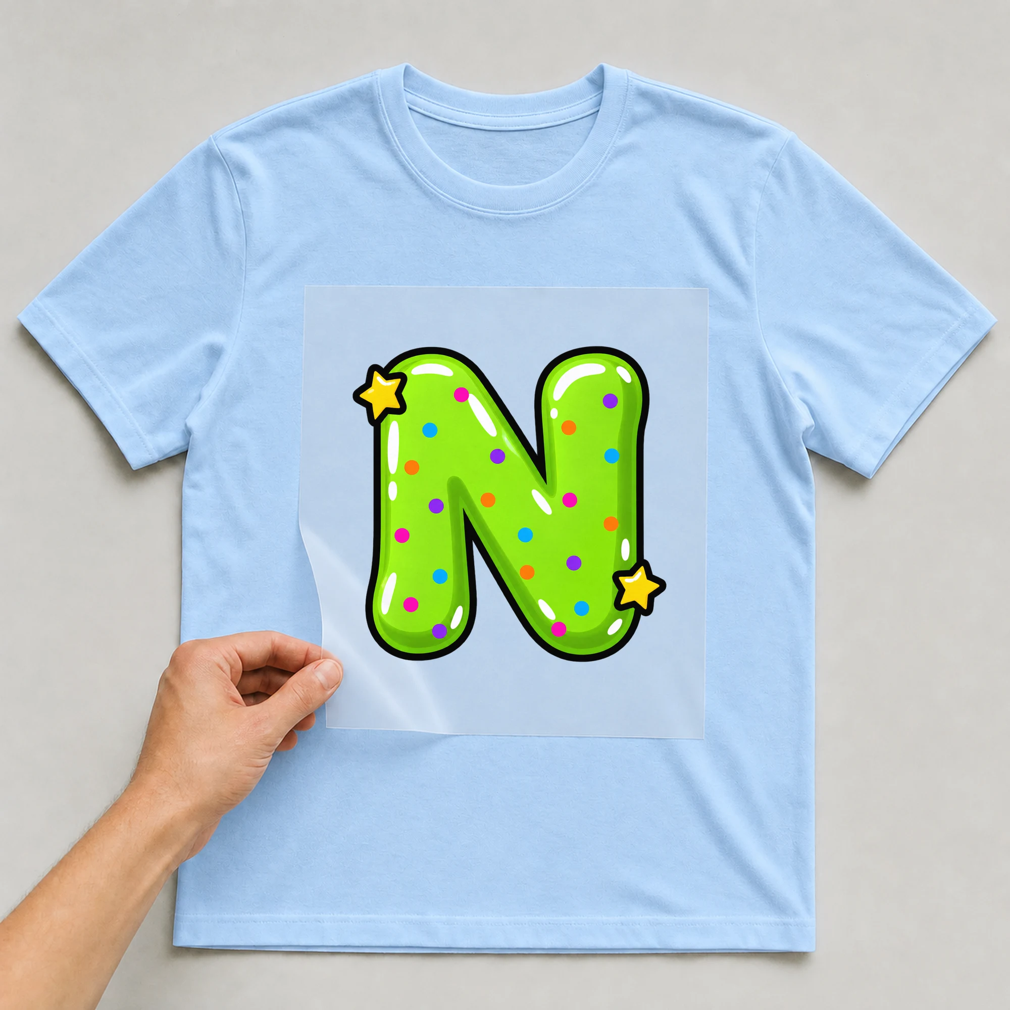 Bügelbild „Buchstabe N im Comic-Ballon-Stil“ auf babyblauem T-Shirt, Folie wird aufgelegt