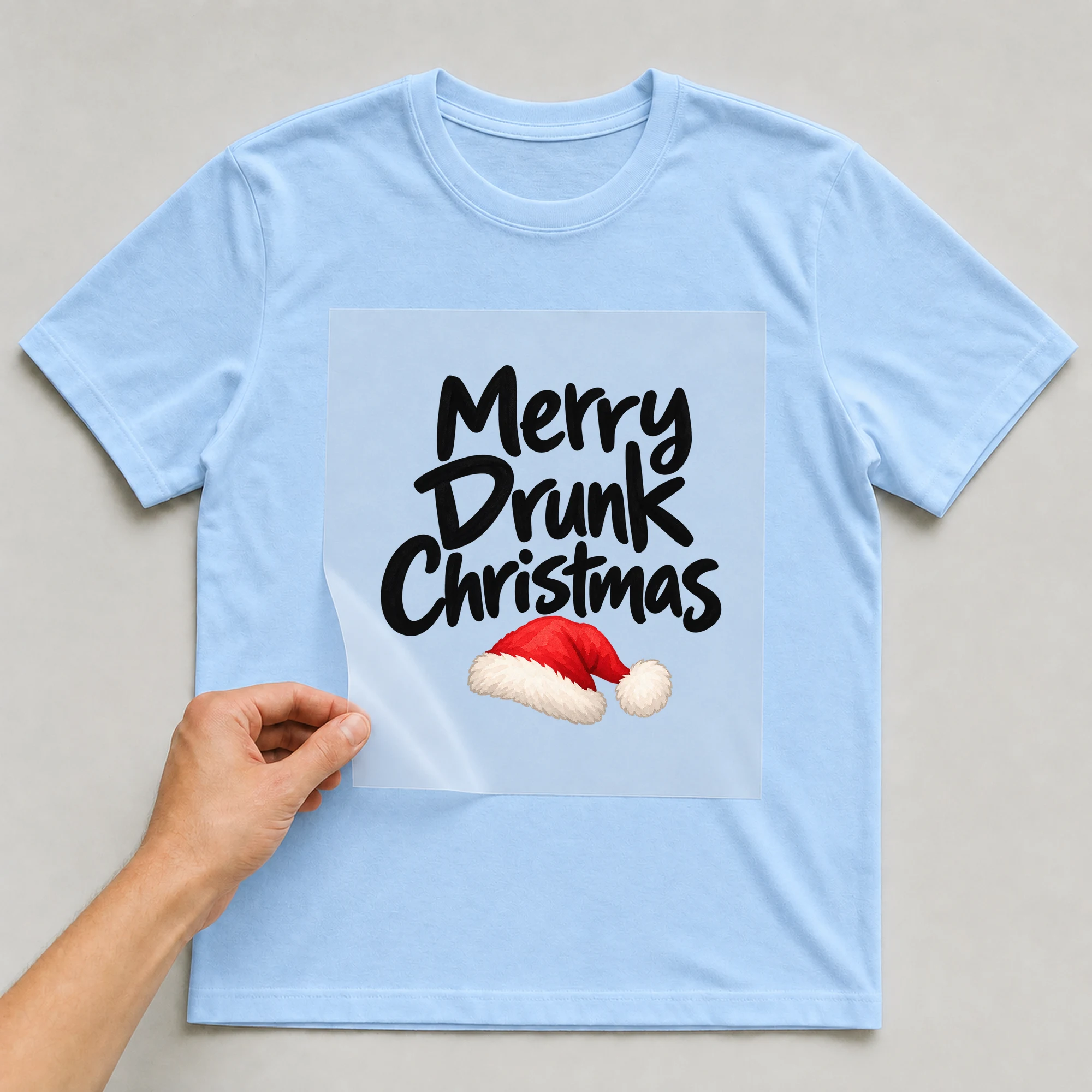 Bügelbild „Merry Drunk Christmas“ auf babyblauem T-Shirt, Folie wird aufgelegt