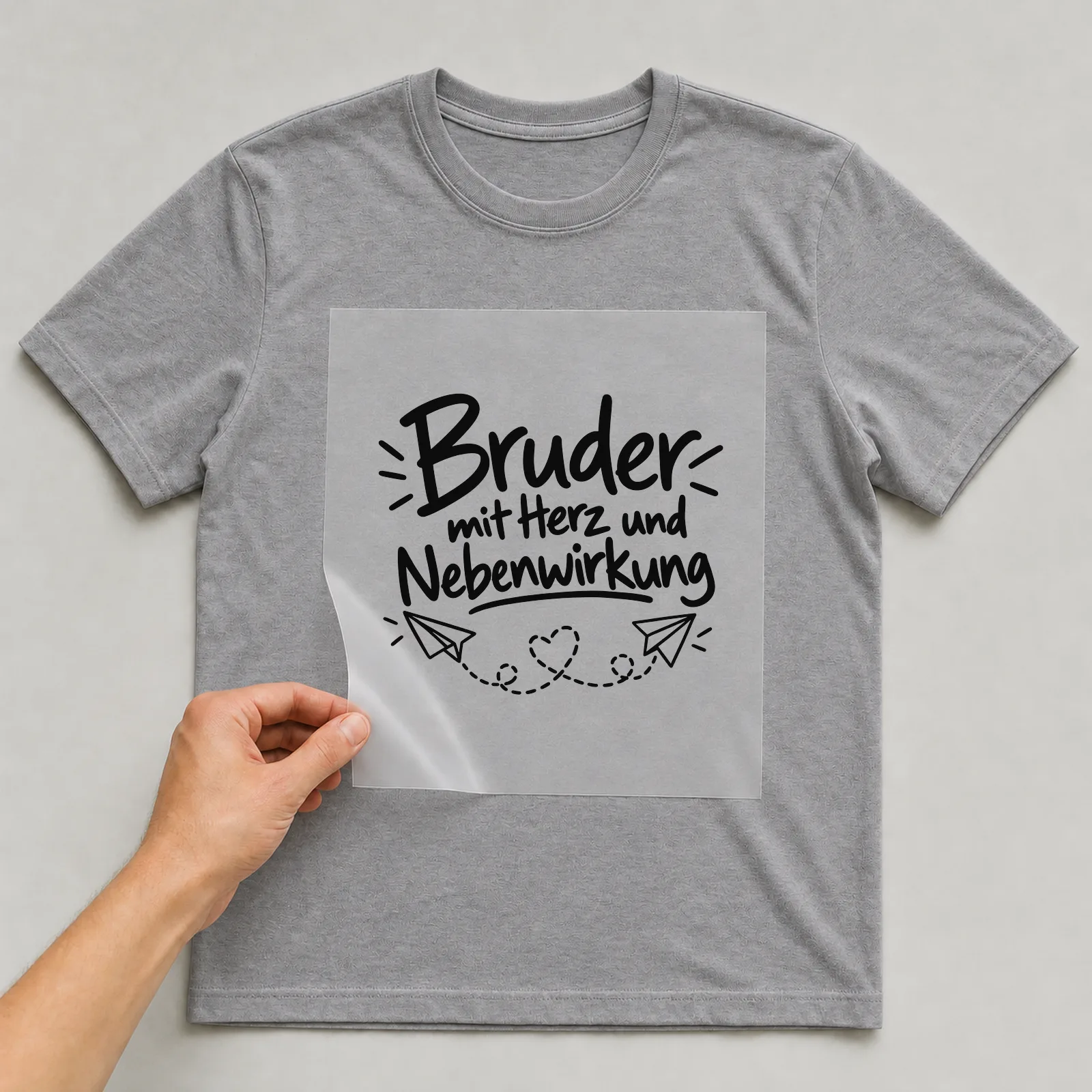 Bügelbild „Bruder mit Herz und Nebenwirkung“ auf grauem T-Shirt, Folie wird aufgelegt