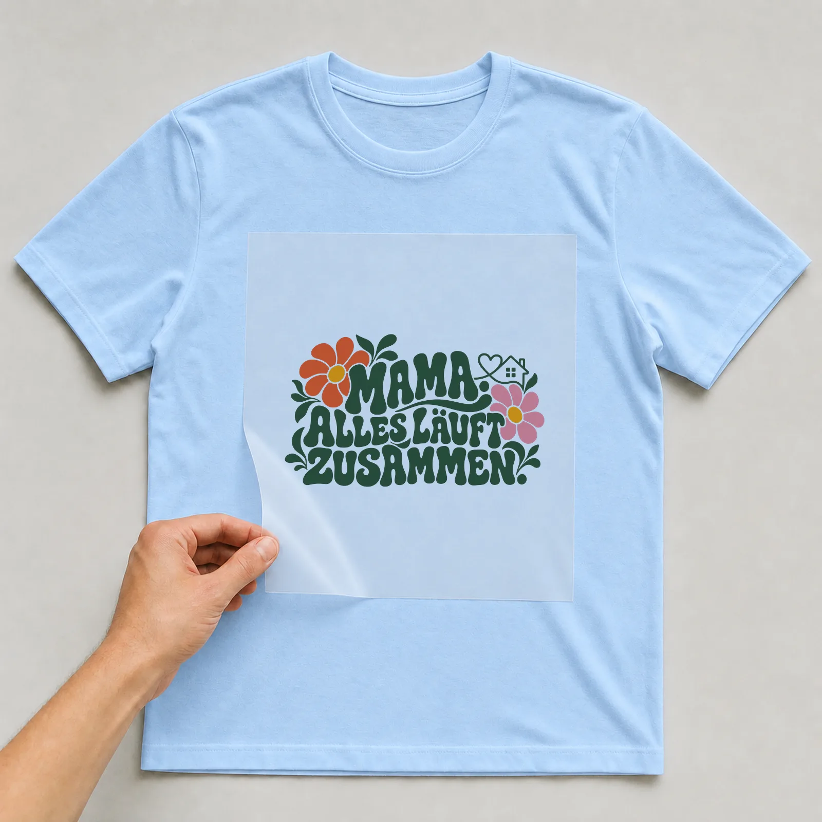 Bügelbild „Mama. Alles läuft Zusammen.“ auf hellblauem T-Shirt, Folie wird aufgelegt